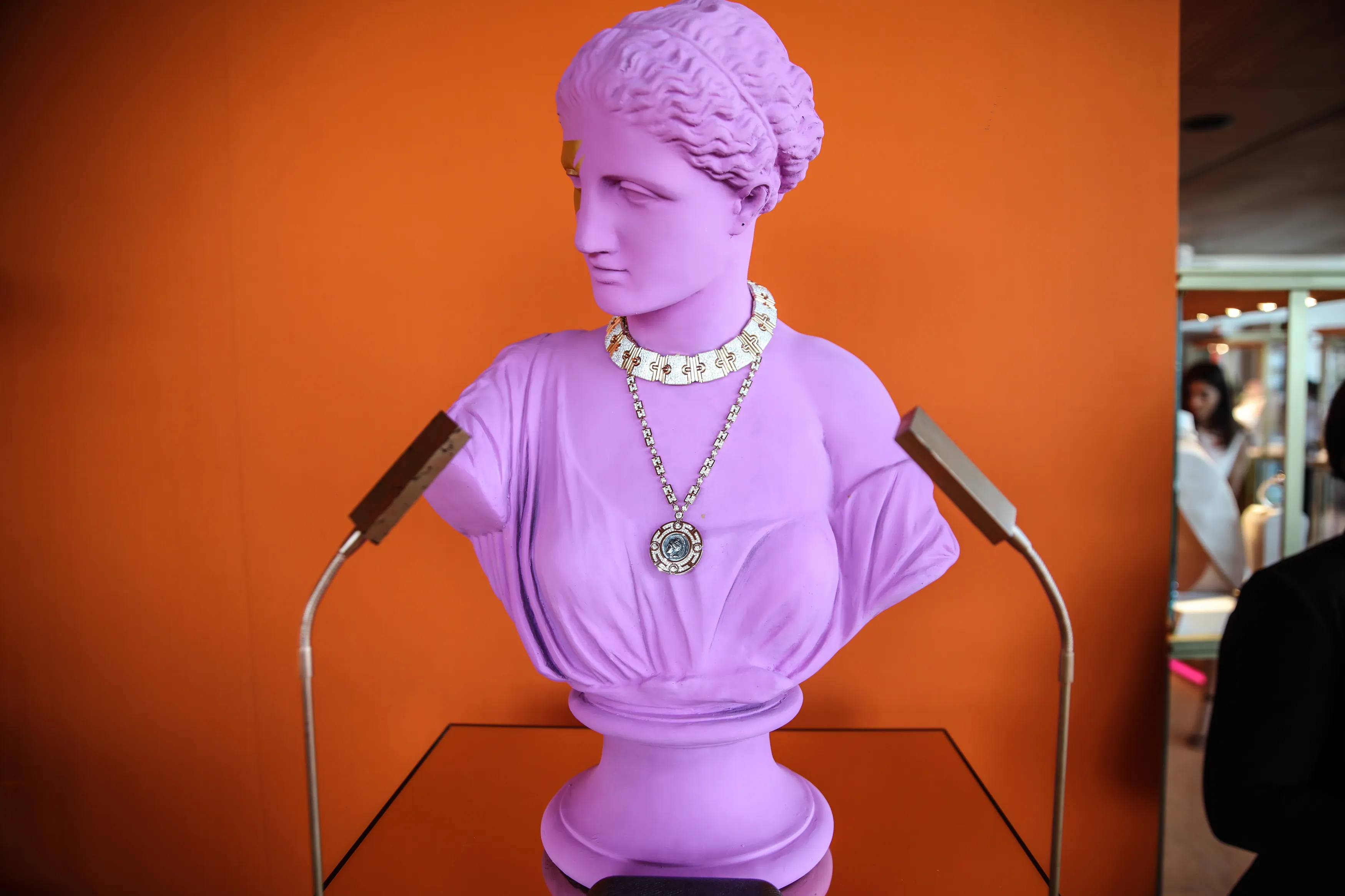 Lilac bust wearing a Bvlgari necklace against orange wall