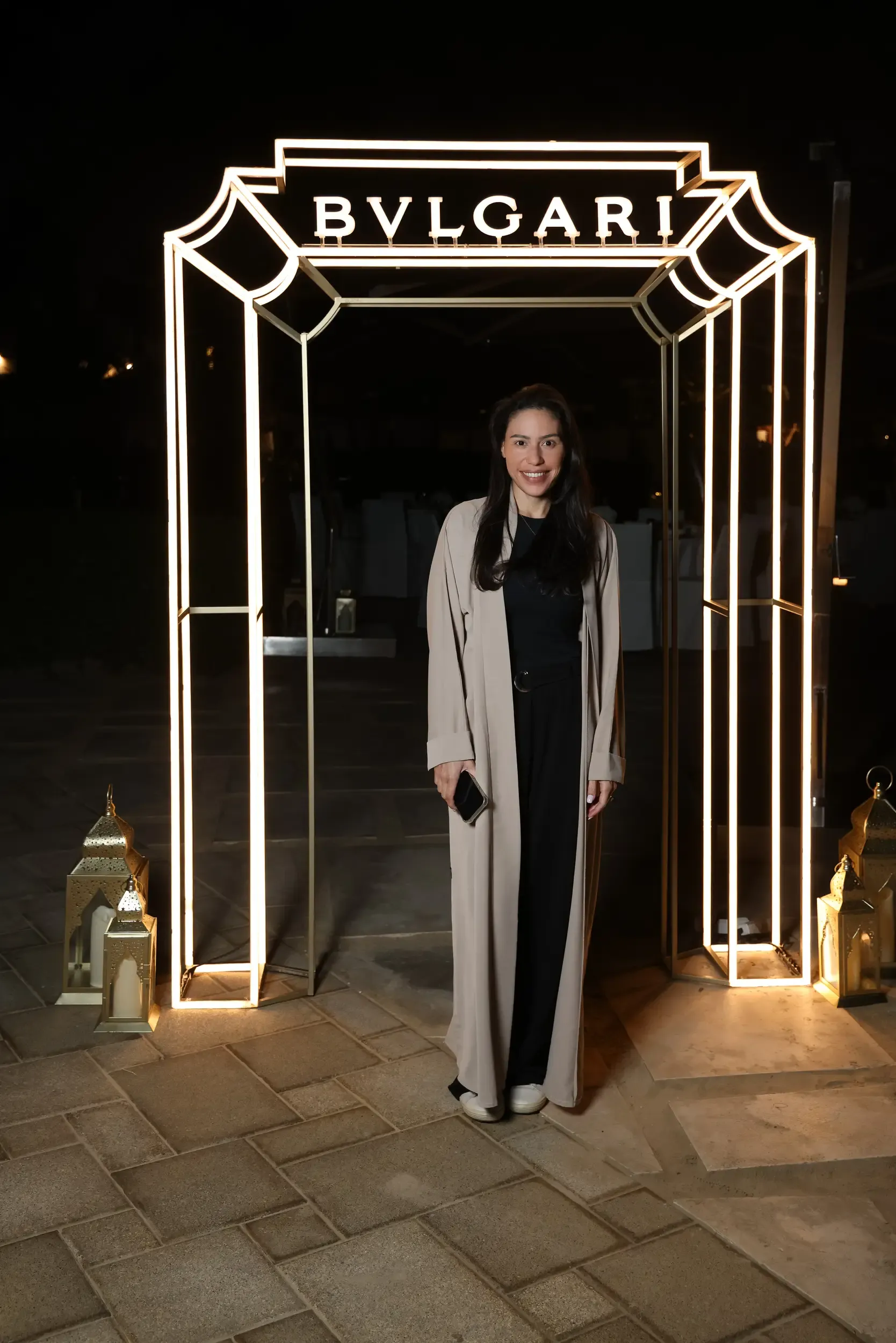 Guest posing inside an illuminated BVLGARI light frame with lanterns at an outdoor night brand event