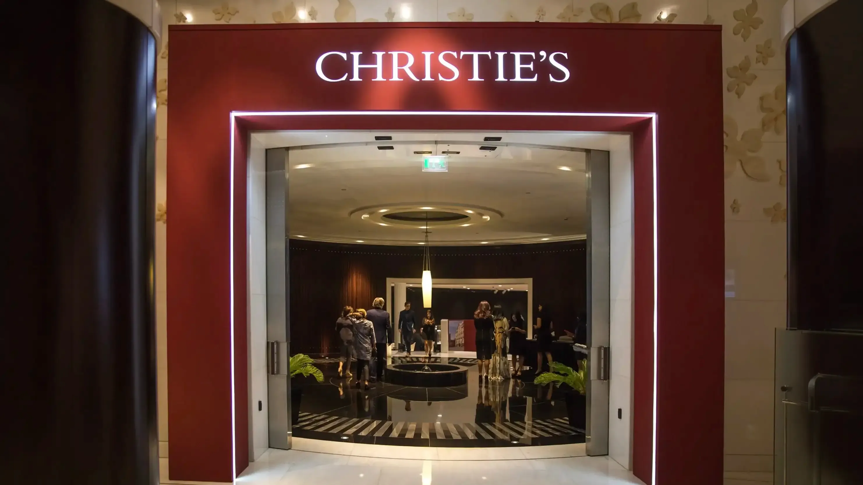 Christie's illuminated red portal entrance looking into a marble lobby with formally dressed guests