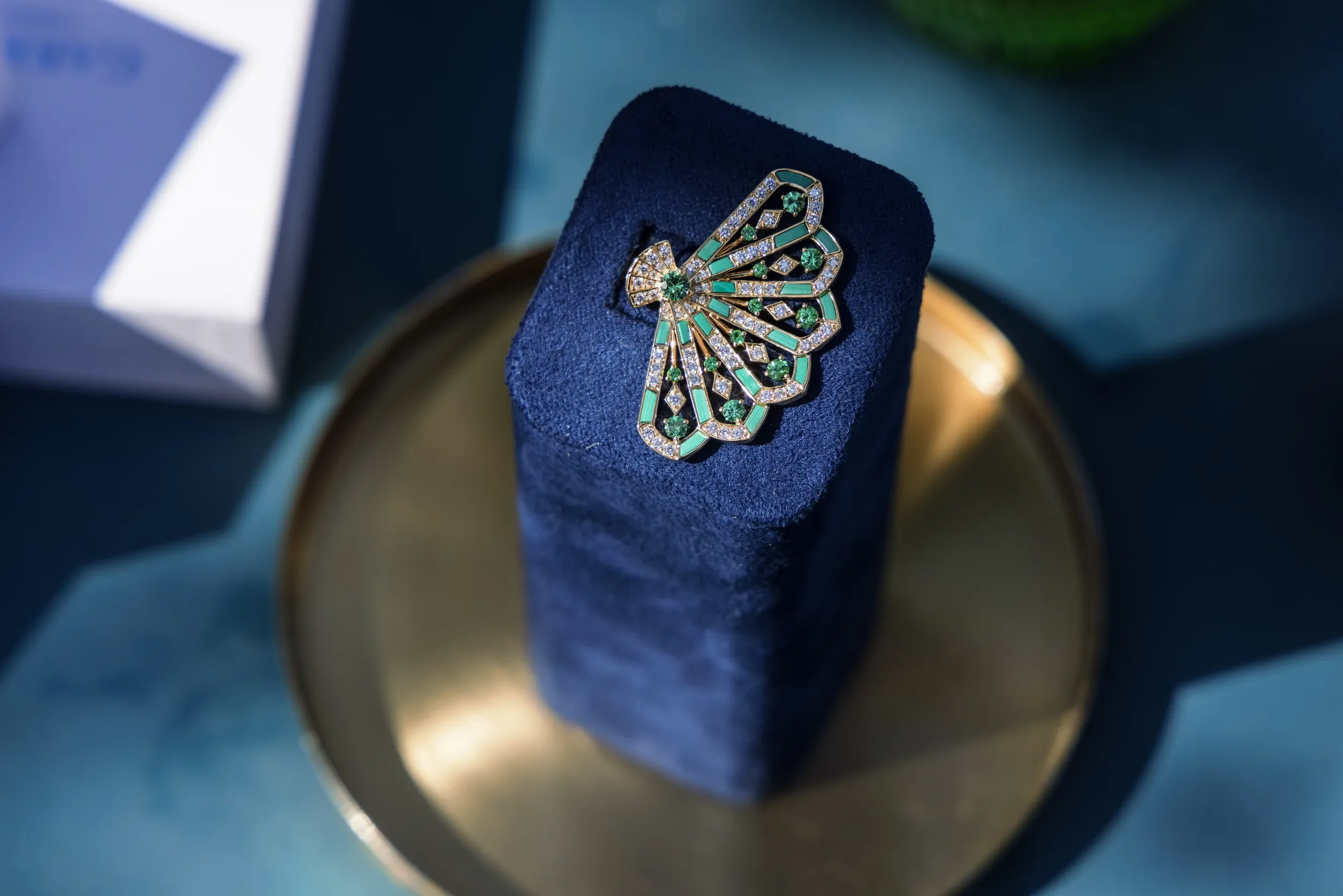 A fan-shaped green and clear gemstone jewel displayed on dark blue velvet.