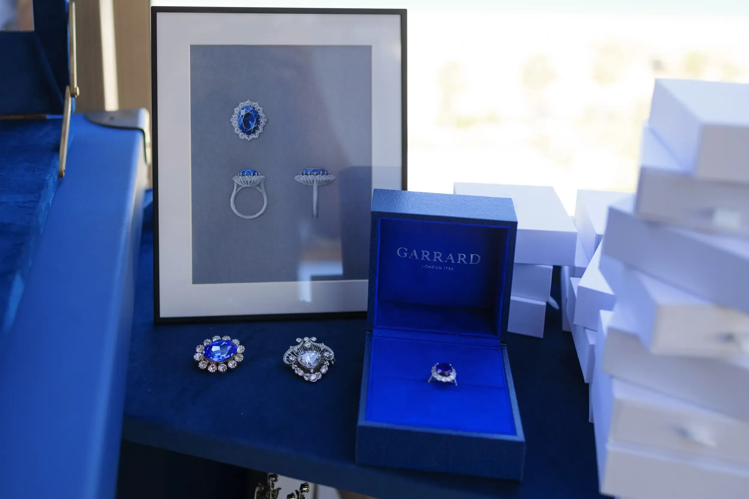 Garrard London sapphire ring and brooches displayed on blue velvet with a design sketch