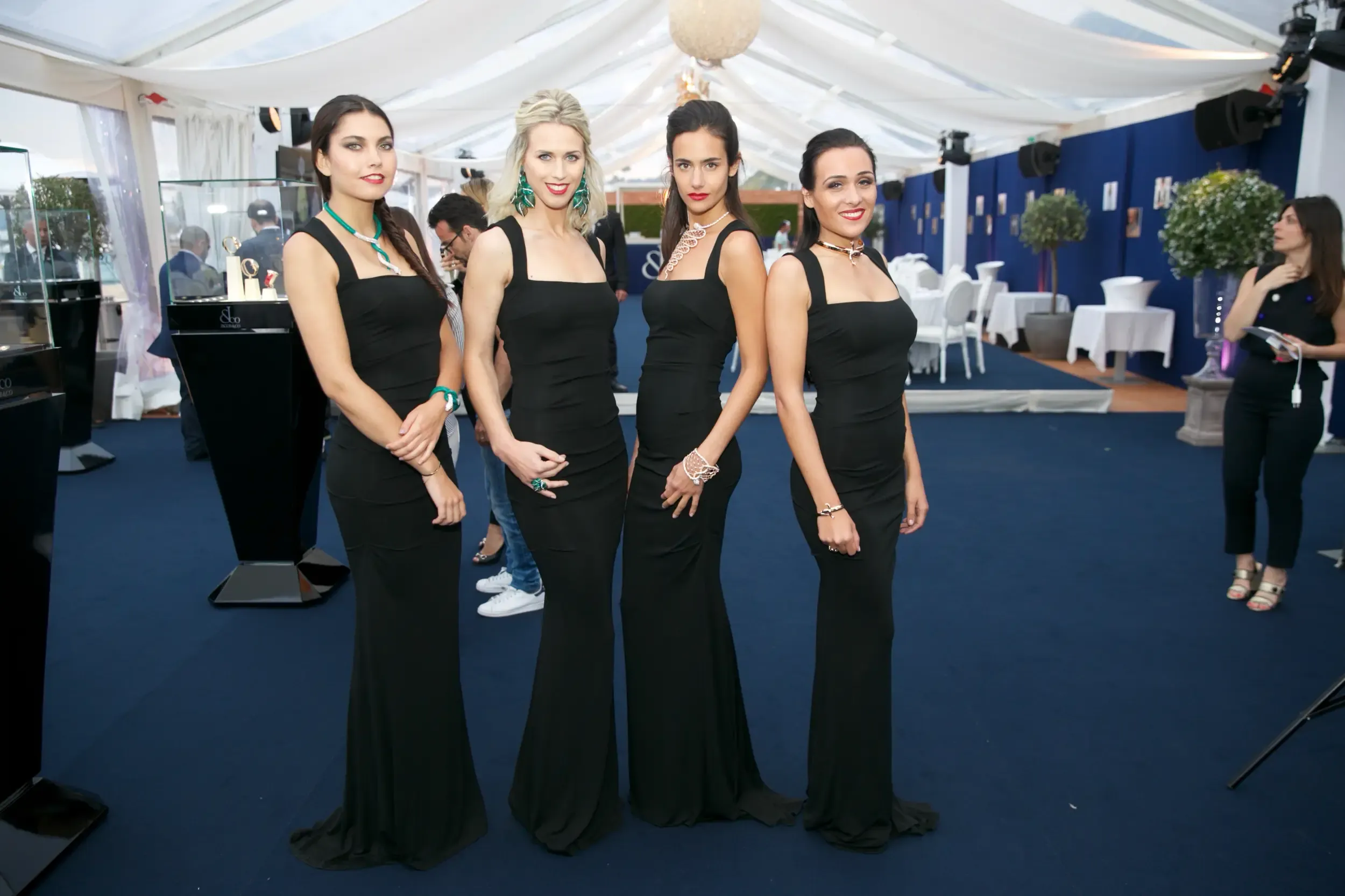 Four hostesses in matching black gowns modelling statement jewelry at a Jacob & Co luxury pavilion event