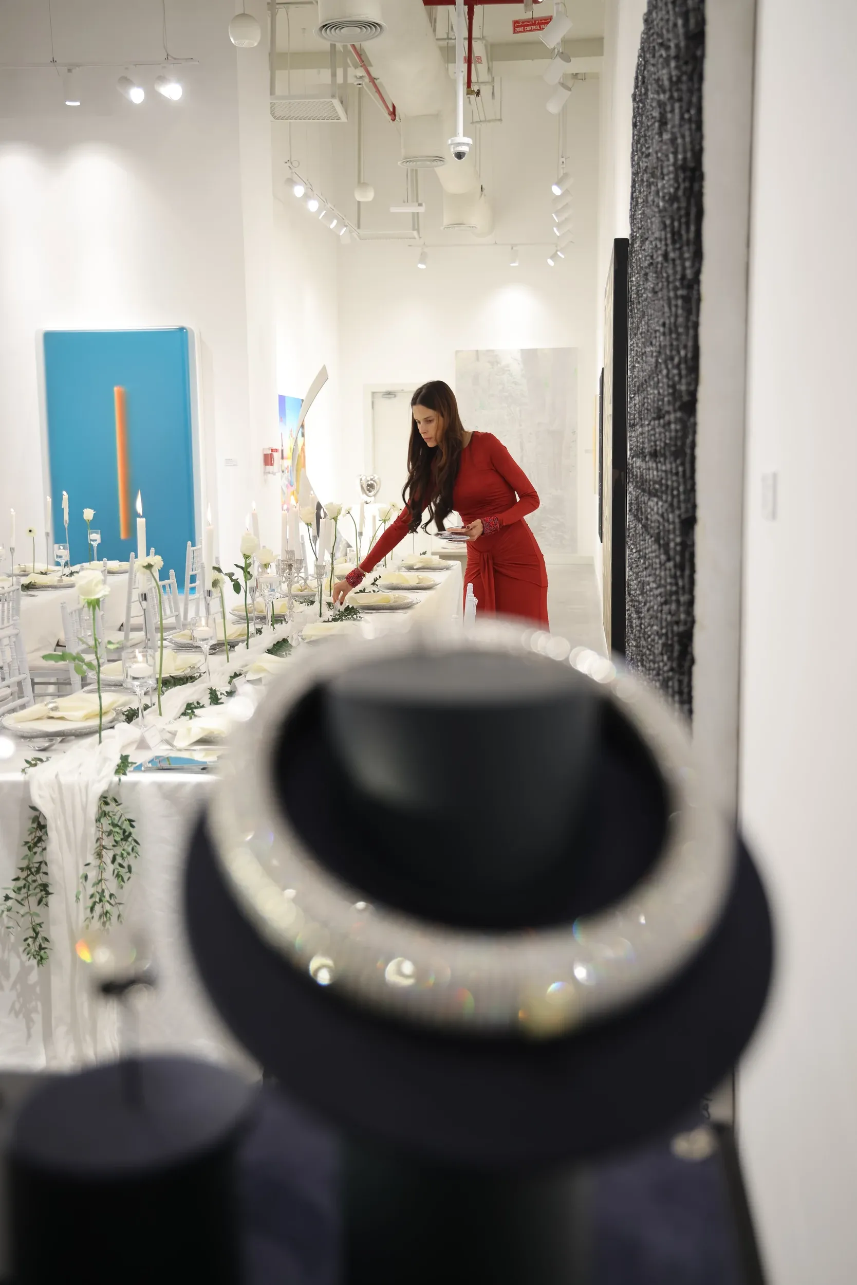 A woman arranging a long table behind a softly blurred jewellery display.