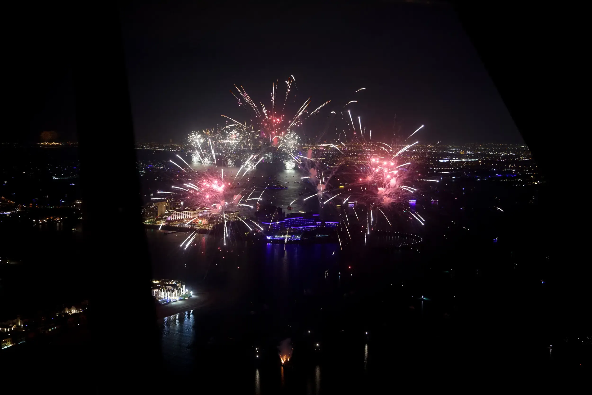 Aerial night view of pink and silver fireworks over Dubai coastline and lit towers
