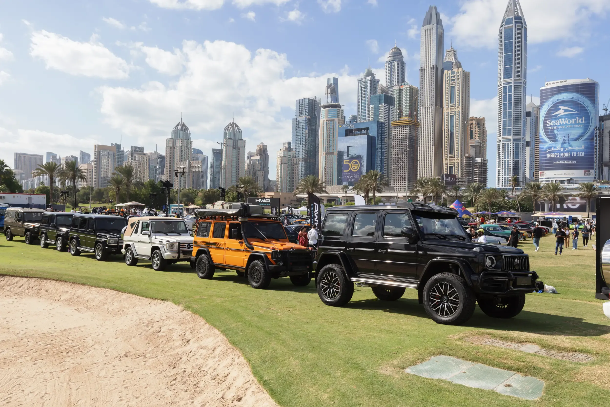 Line of Mercedes G-Class SUVs on a lawn with Dubai Marina skyline behind at a luxury car meet