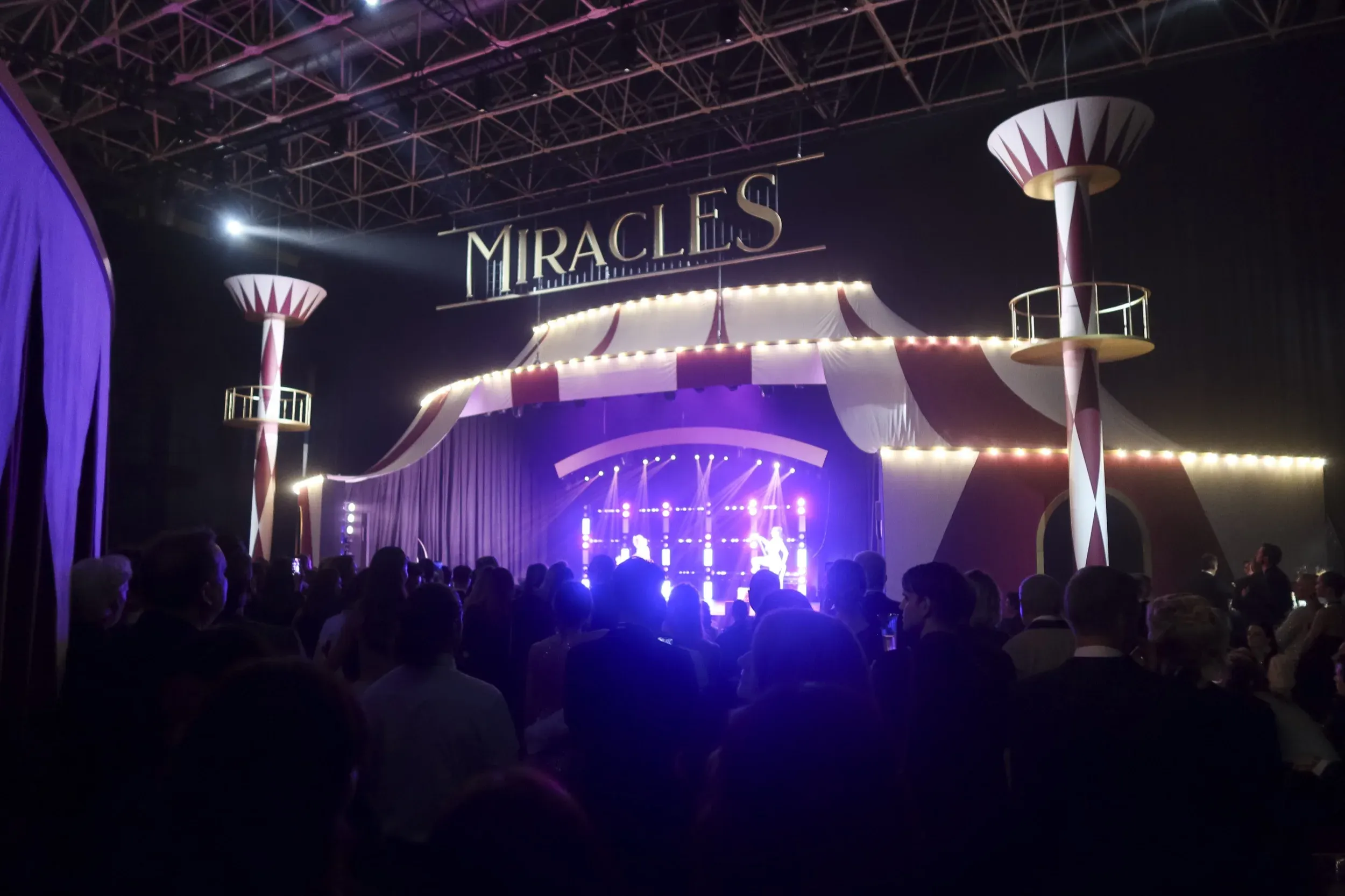 Crowd facing the Miracles circus-themed stage with red-and-white striped big-top set and purple spotlights