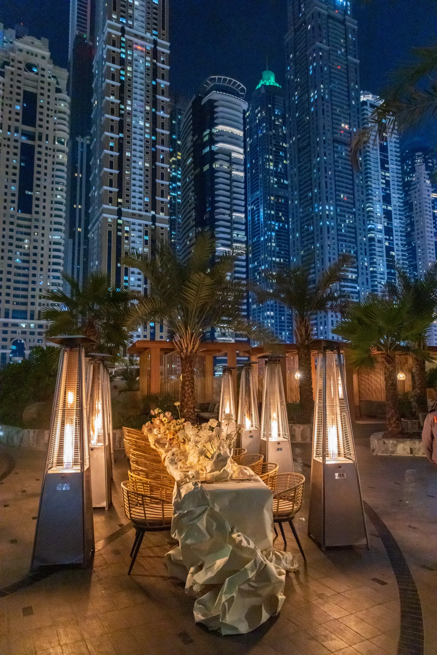 A candlelit outdoor dining table beneath illuminated high-rise buildings.
