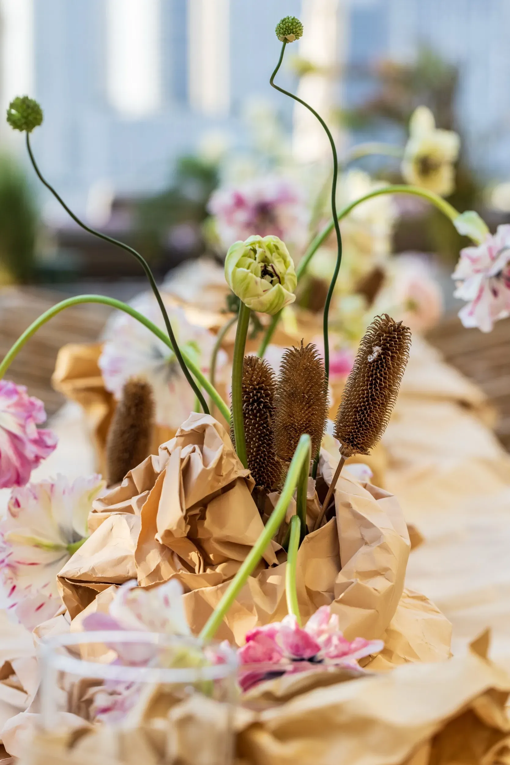 Artistic floral centerpiece with pink ruffled blooms and dried seed pods in crumpled craft paper