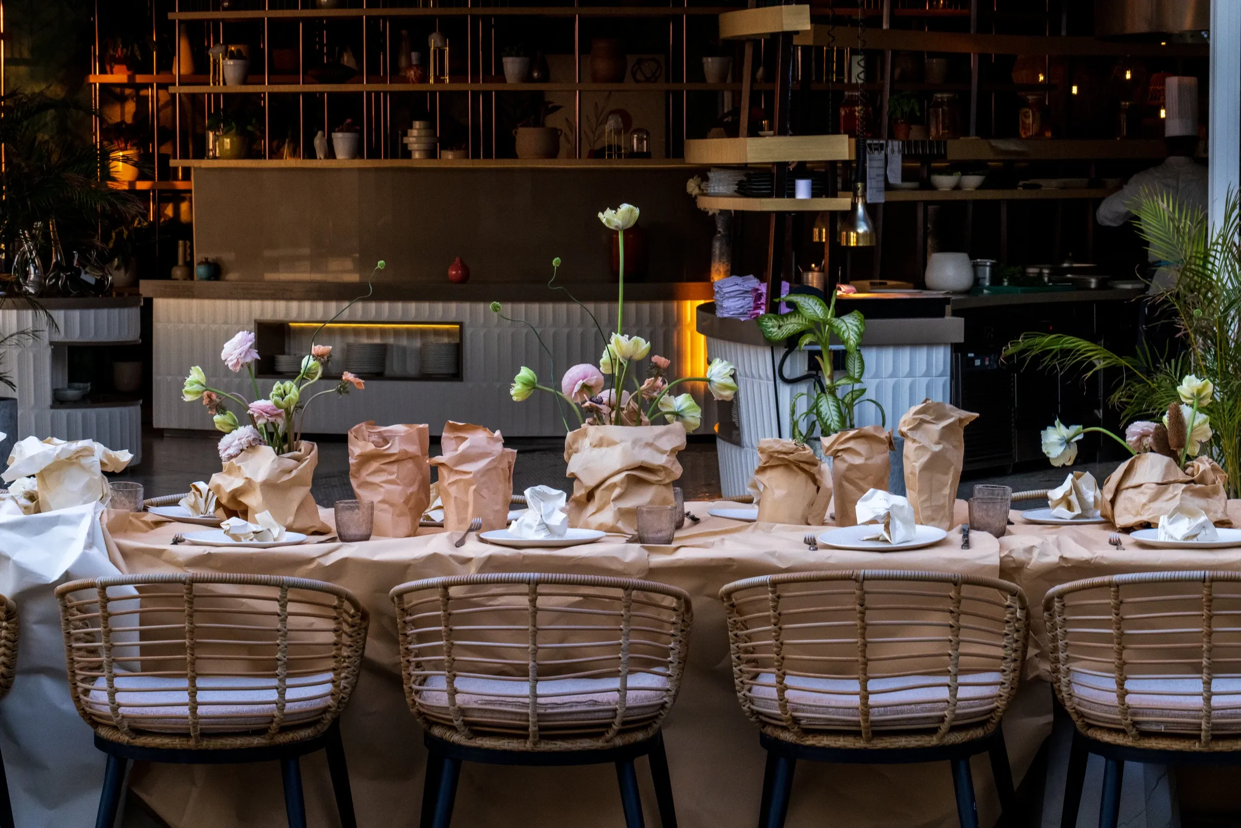 A flower-dressed dining table viewed across woven chairs toward a bar.