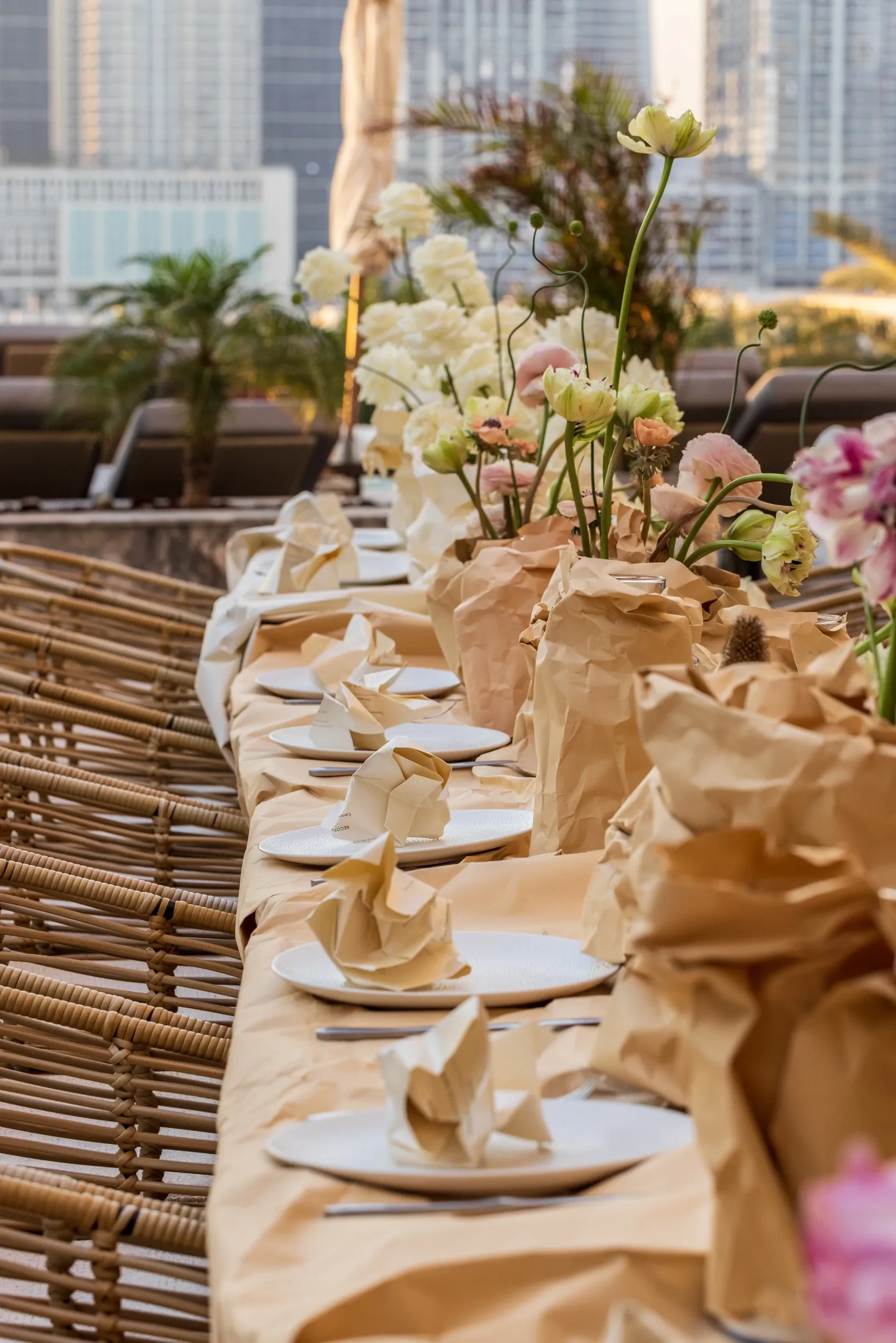 A long outdoor table dressed with pale settings and tall floral arrangements.