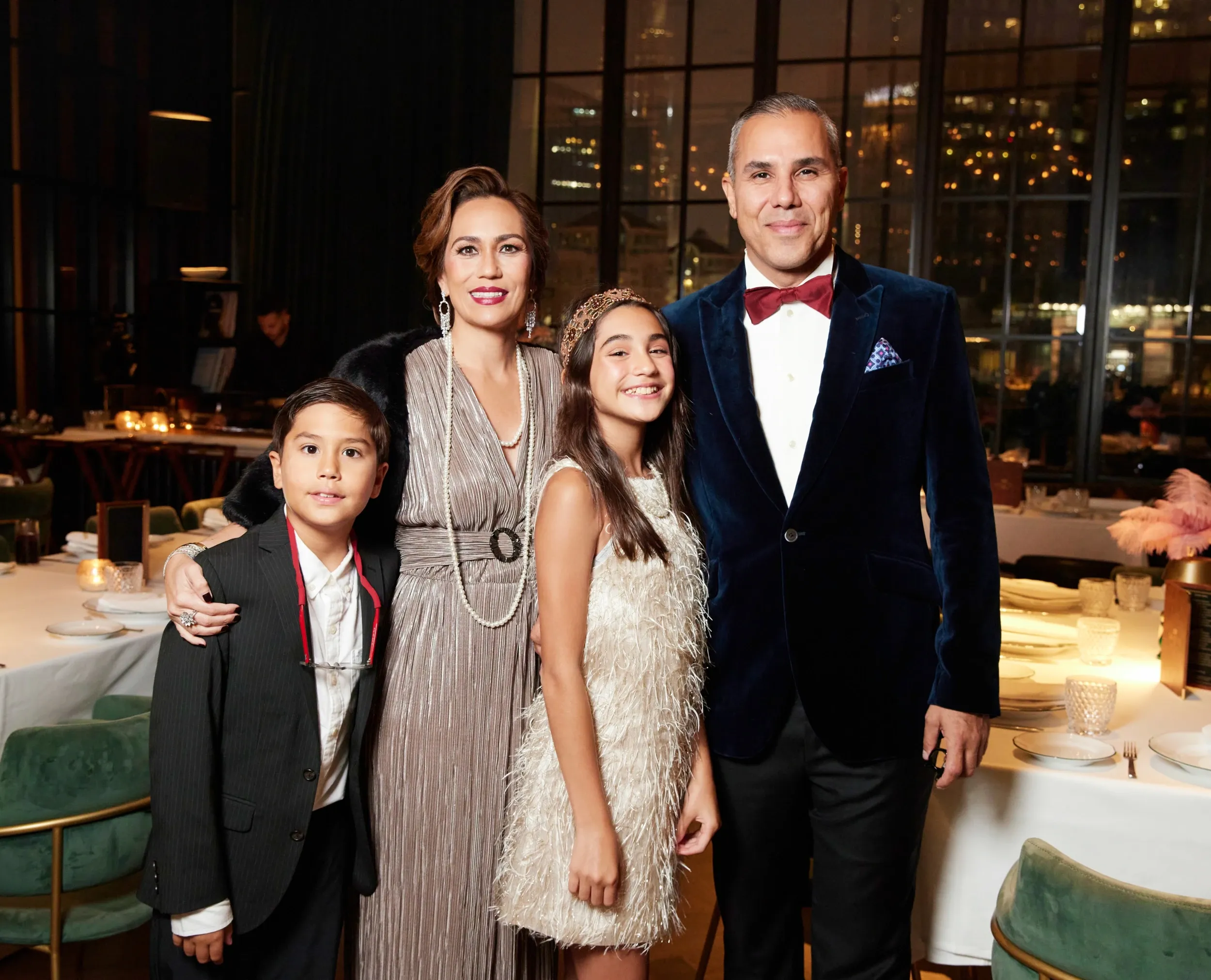 Two adults and two children in formal clothing posing at an evening celebration.