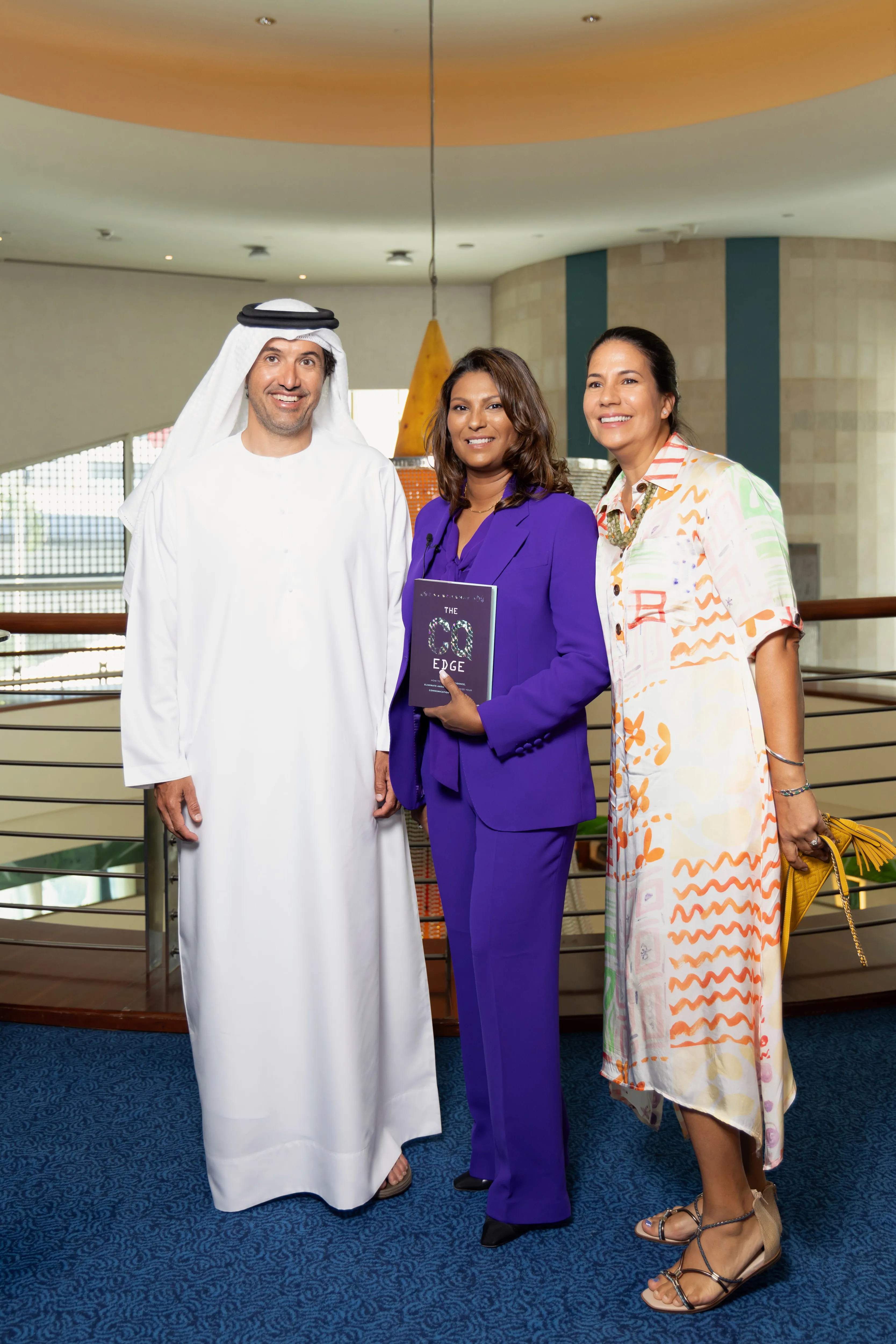 Three executives, one in kandura holding a book, hotel atrium