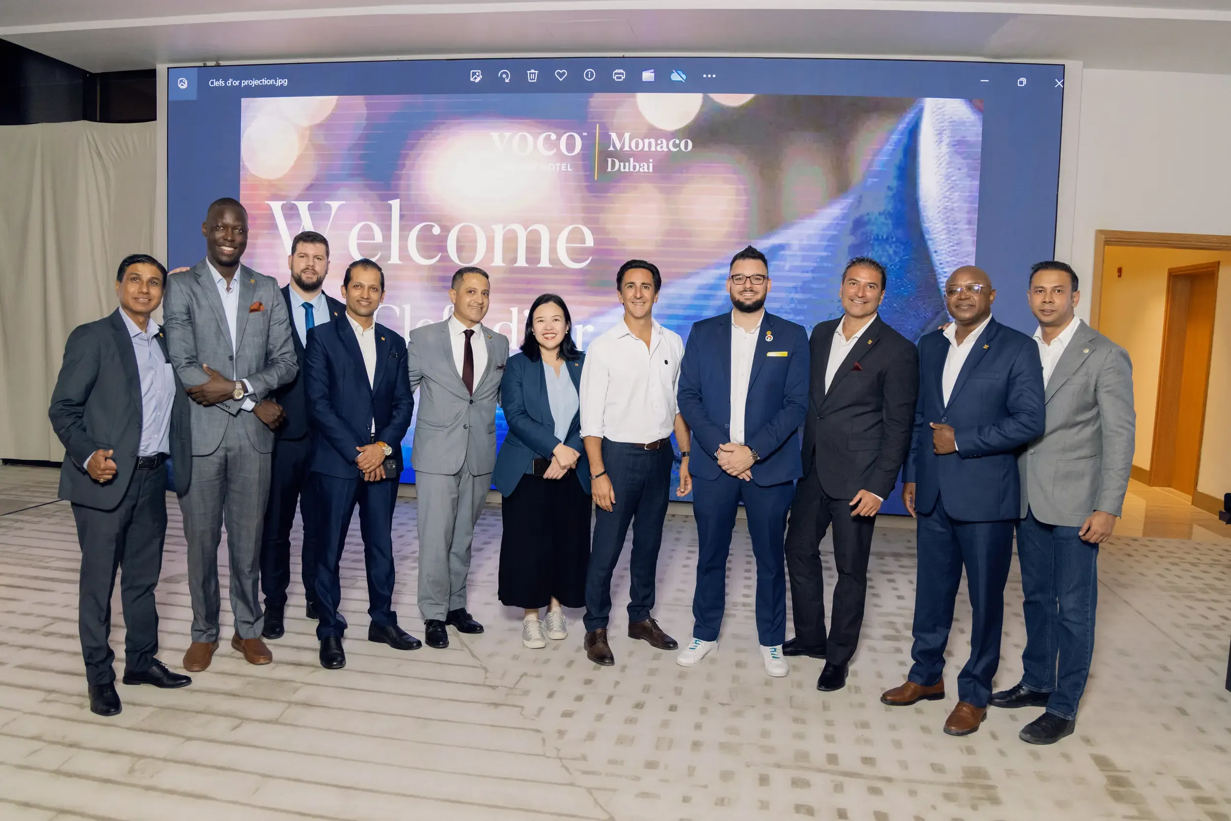 A formally dressed group in front of a Les Clefs d'Or welcome screen.