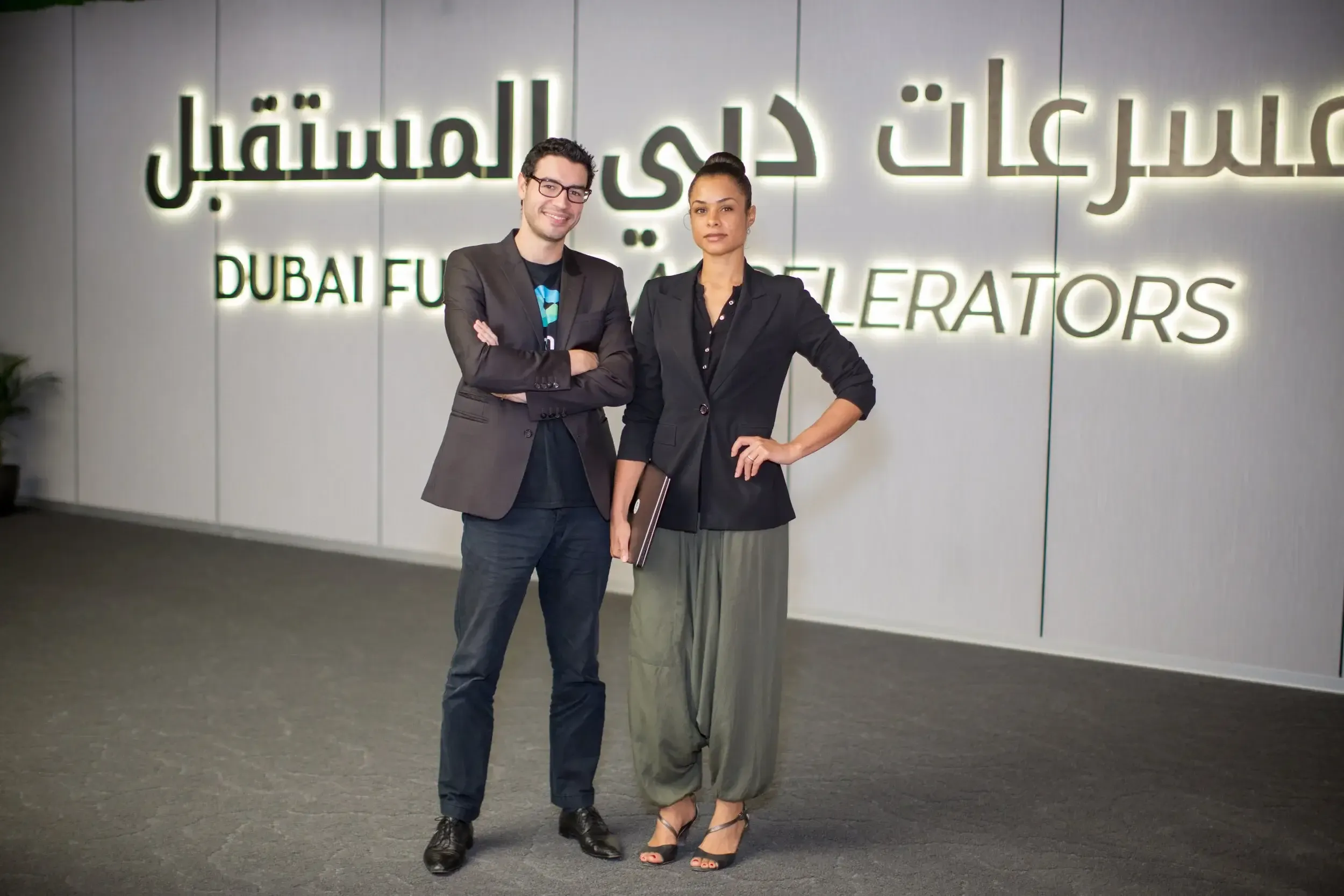 Man and woman posing in front of the Dubai Future Accelerators bilingual backlit sign