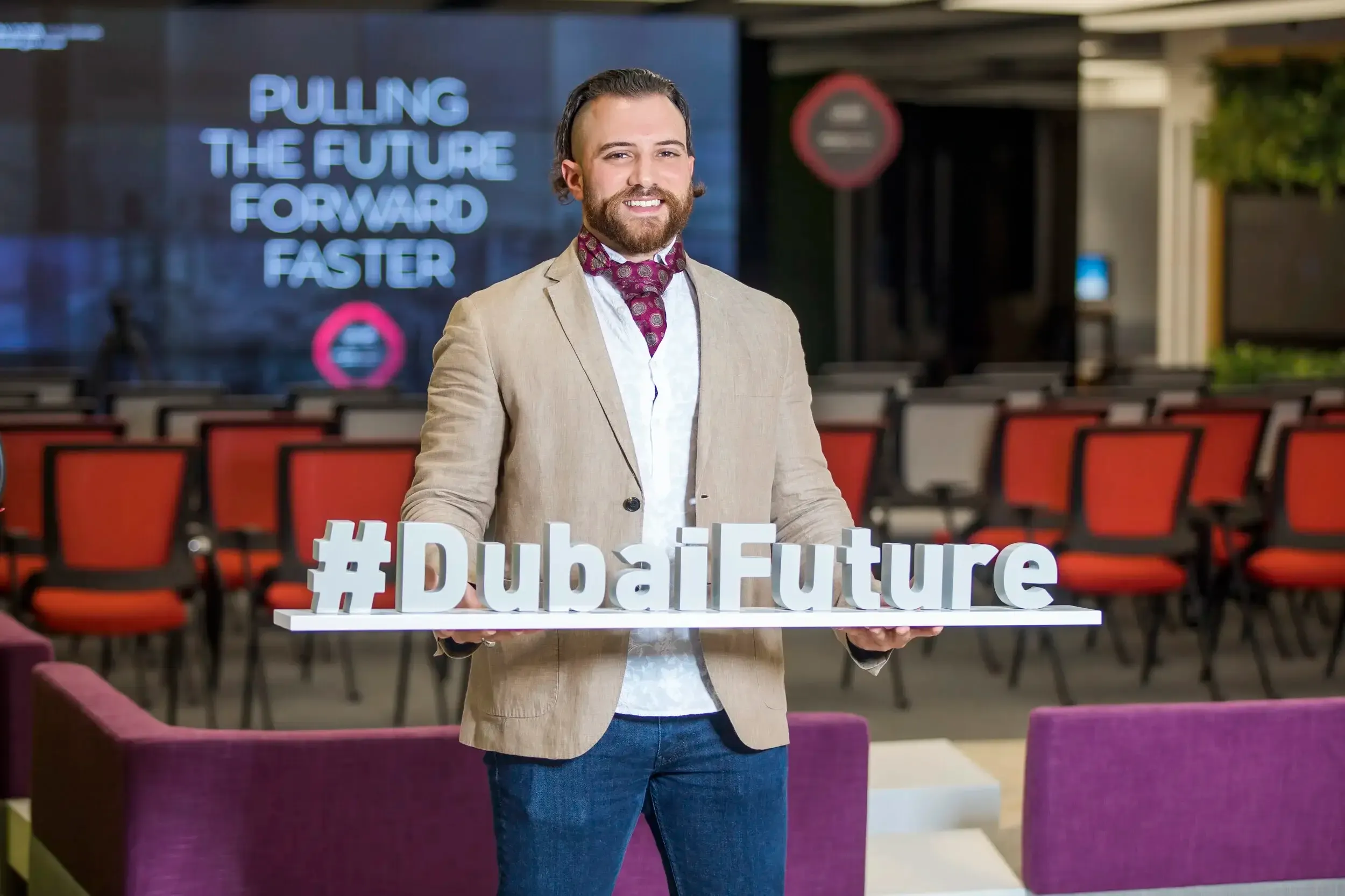Smiling guest in beige blazer holding a #DubaiFuture 3D sign in a conference hall
