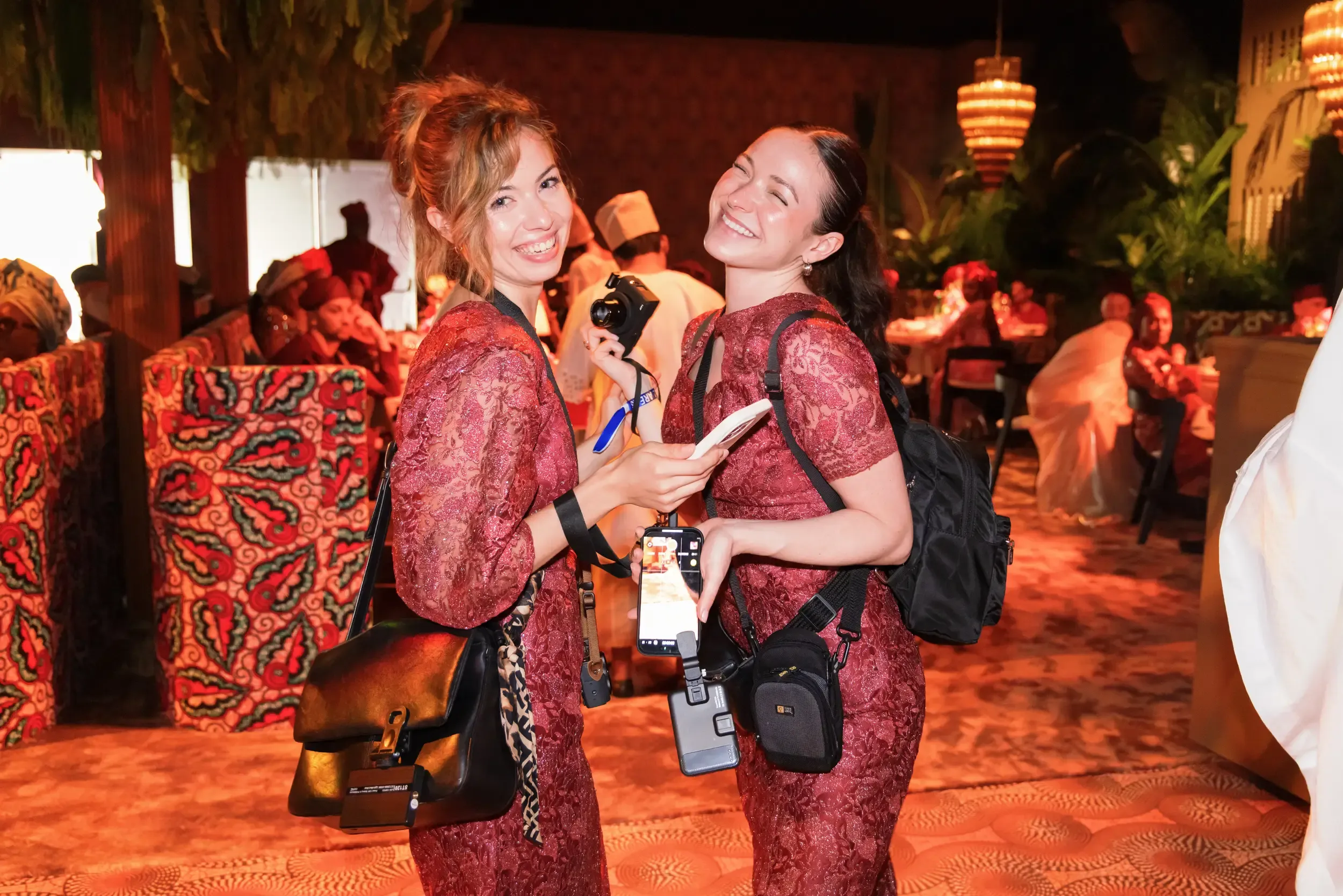 Two female media creatives in matching burgundy lace dresses with camera and gimbal at a luxury gala