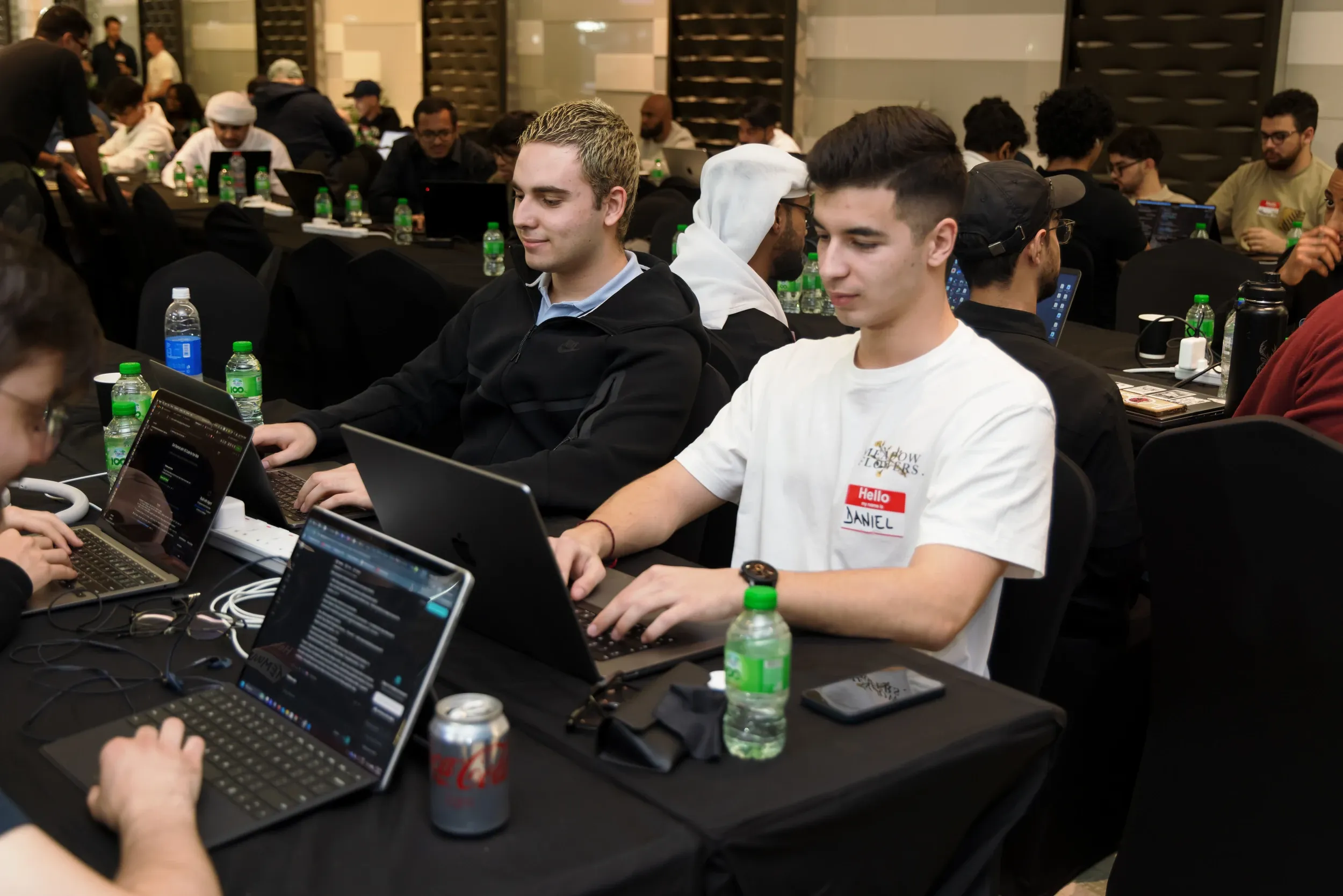 Two participants working at laptops amid a busy group workshop.