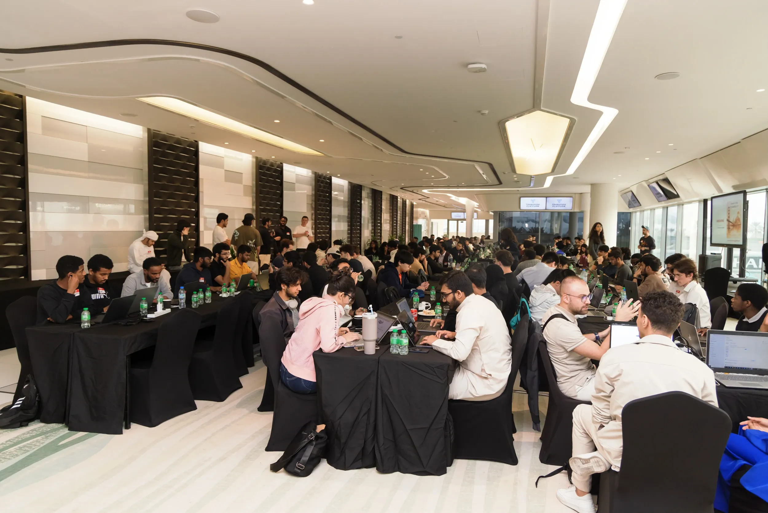 A large room of participants working at laptops around black-covered tables.