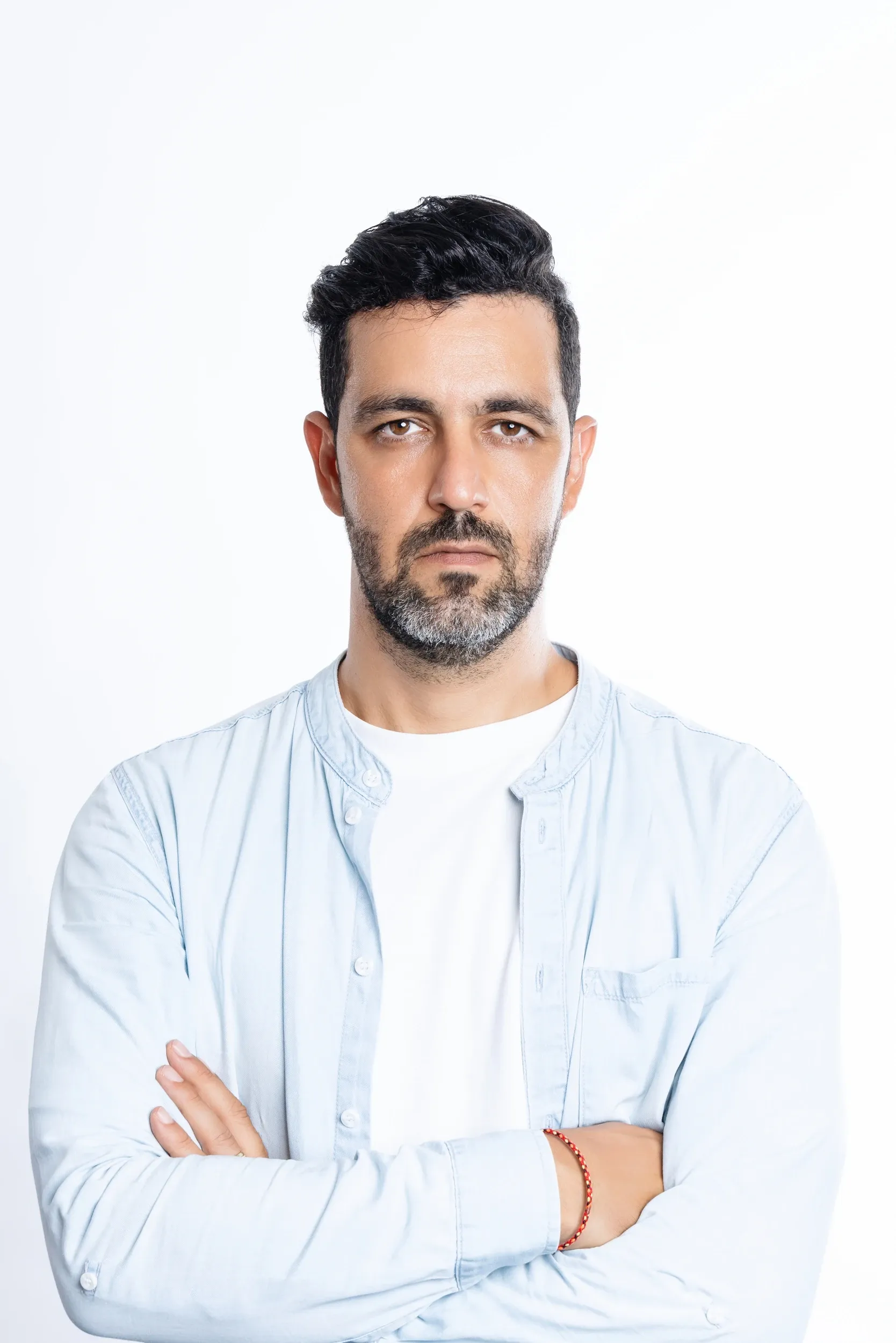 A man in a pale overshirt with folded arms against a clean white background.