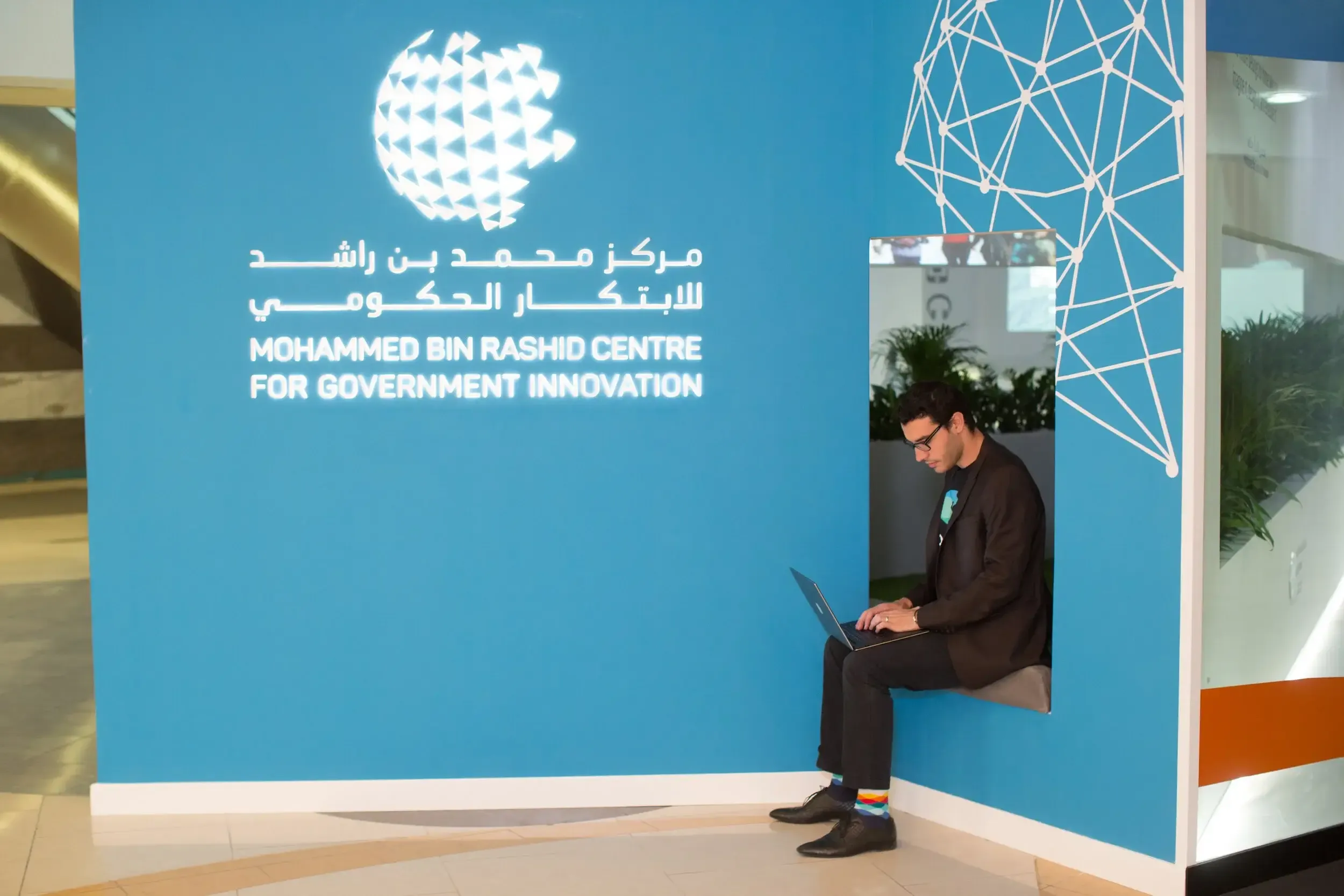Innovator working on a laptop in a blue branded nook at the Mohammed Bin Rashid Centre for Government Innovation