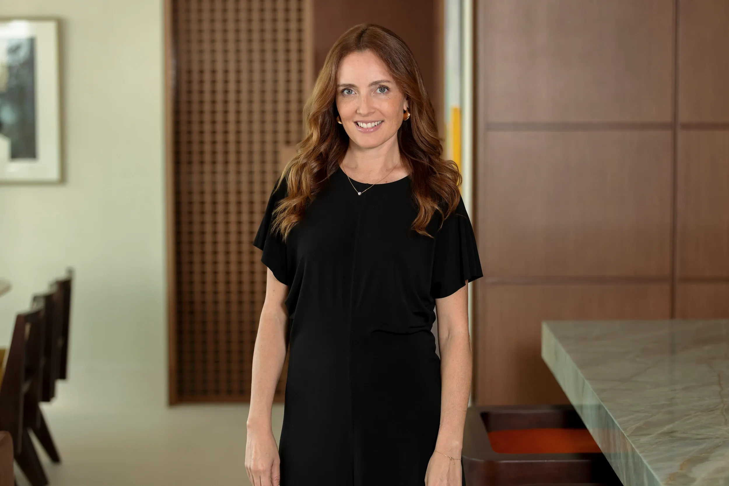 A smiling woman in a black dress standing in a contemporary interior.