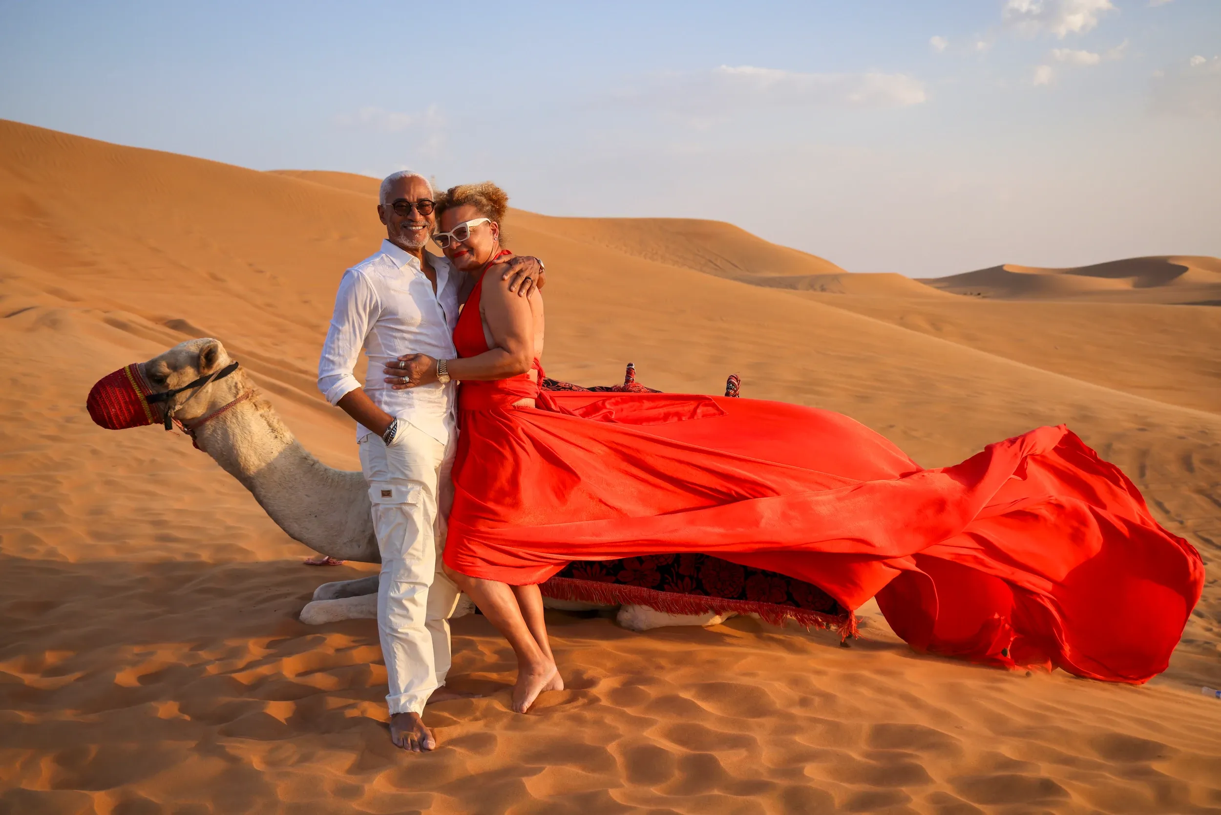 Couple with camel and billowing red dress on dunes