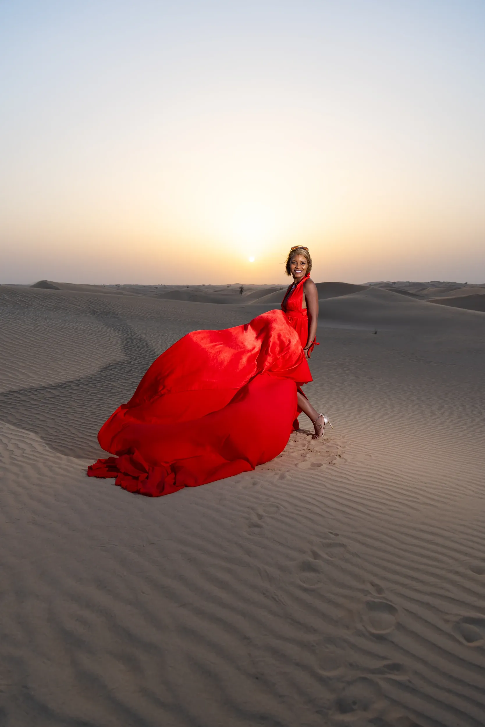 Red dress lifted against setting sun on dunes