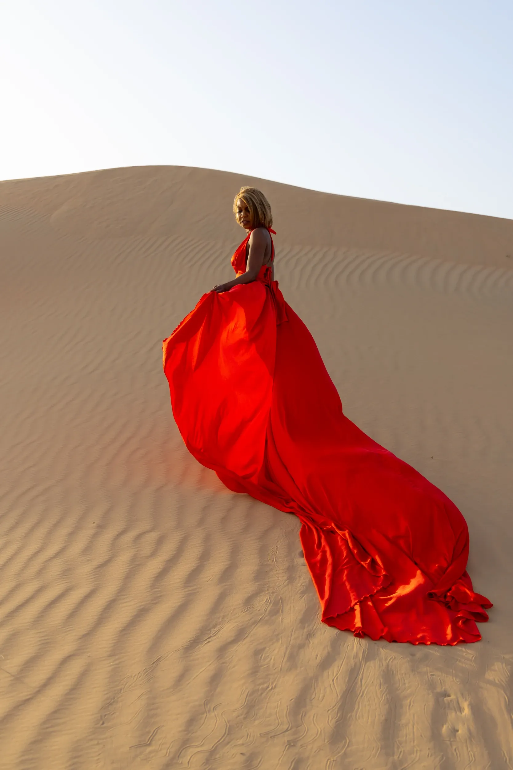 Long red dress on rippled dunes from behind