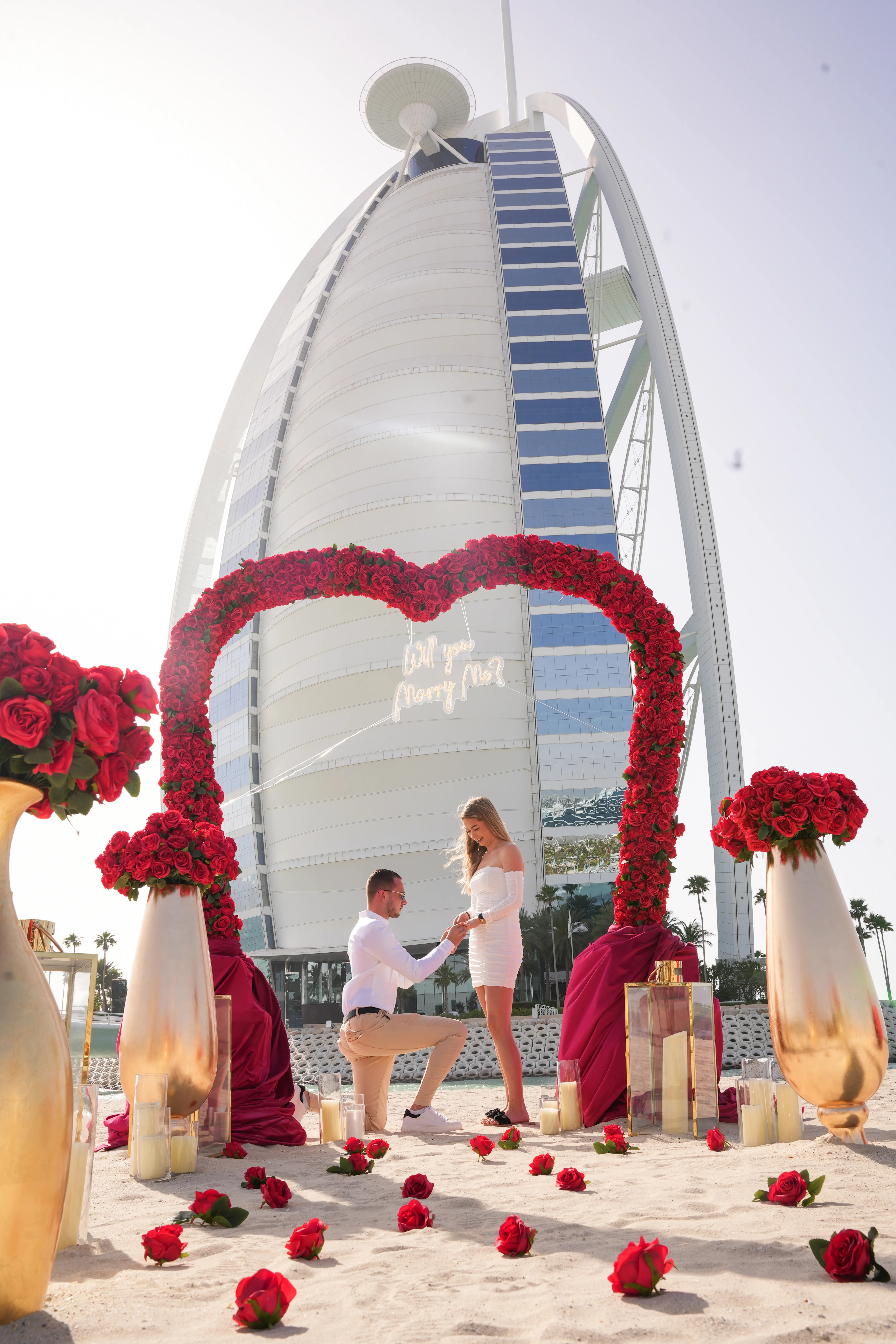 A proposal beneath a red floral arch with the Burj Al Arab behind.
