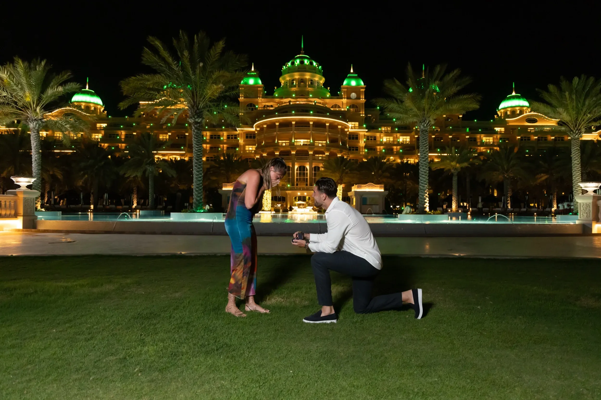 Night proposal on the lawn before an illuminated palatial Dubai hotel with green-lit domes