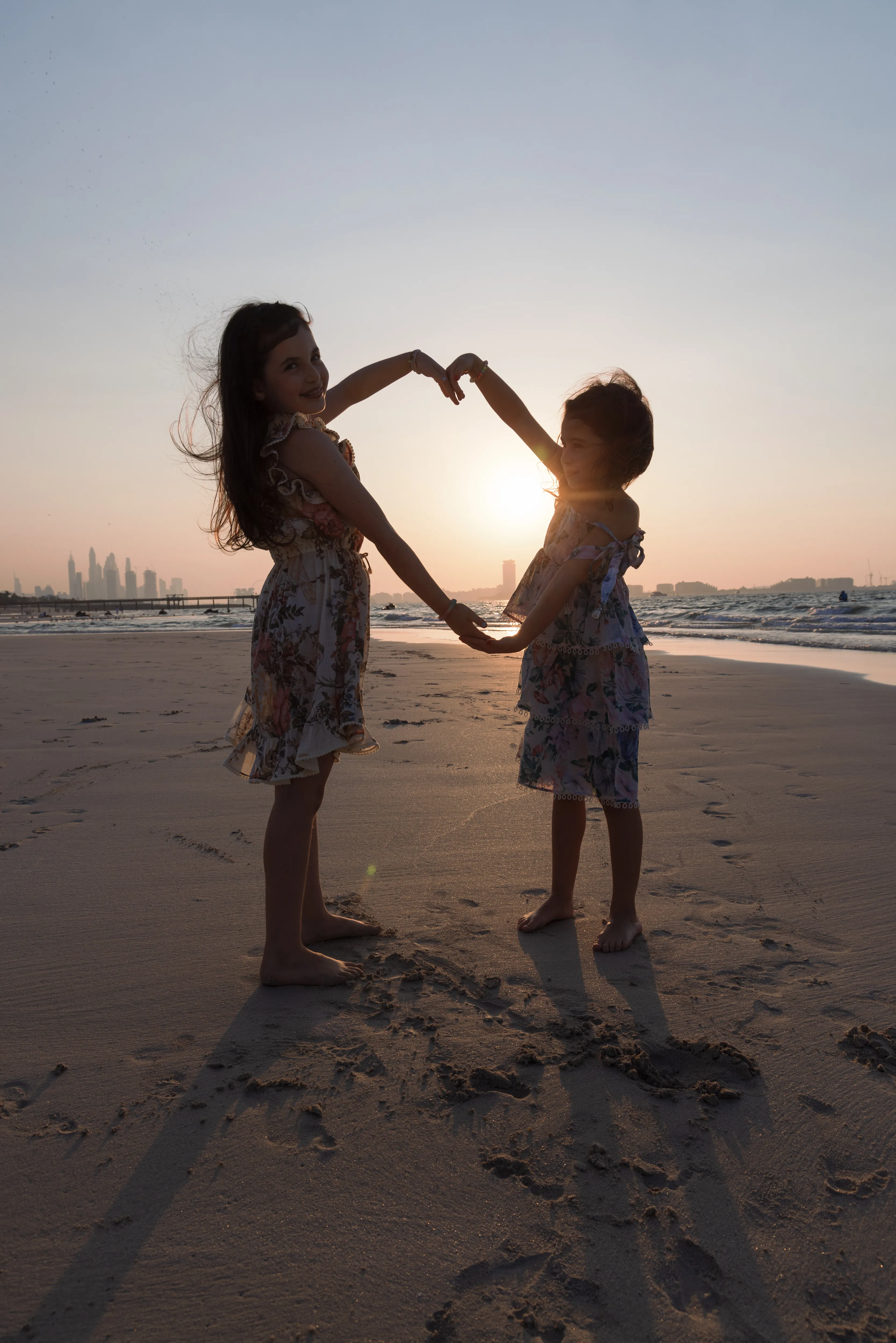 Two children forming a heart at sunset