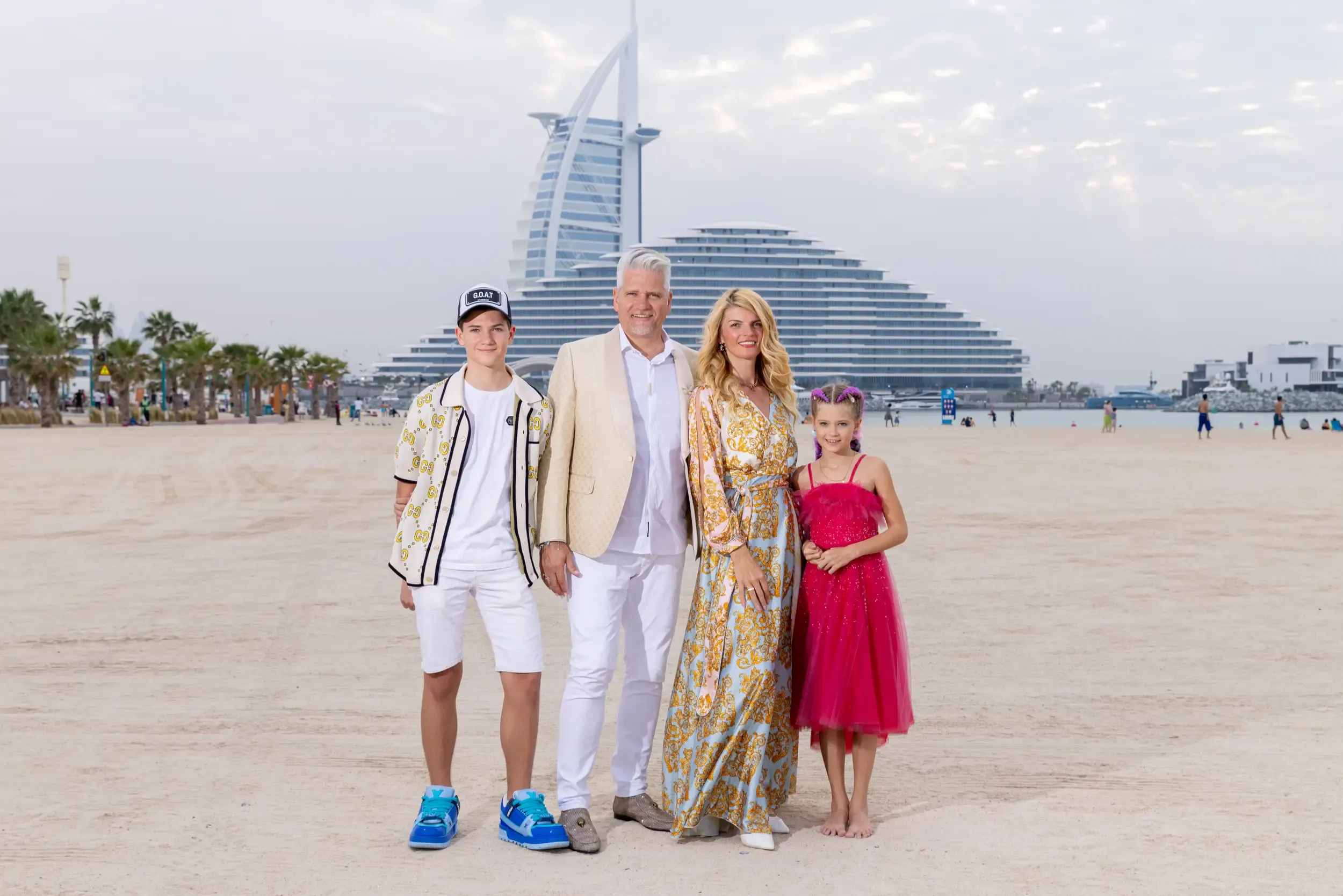 Family of four in coordinated cream and pink outfits on the sand with Burj Al Arab and Jumeirah Beach Hotel behind