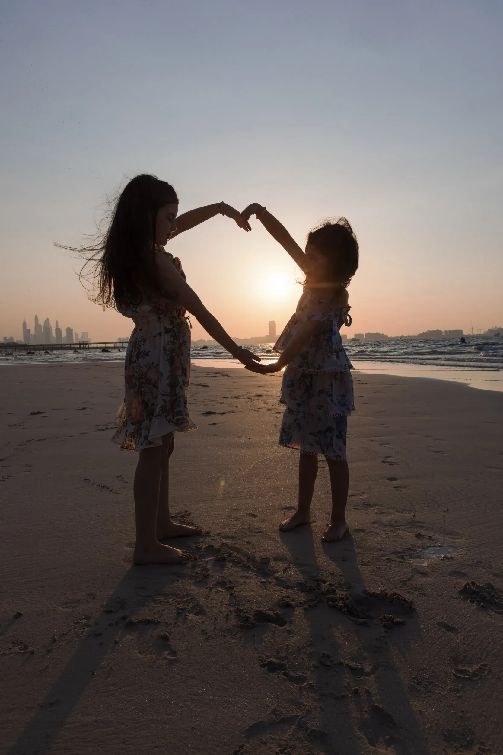 Two girls forming a heart with their arms around the setting sun on a Dubai beach