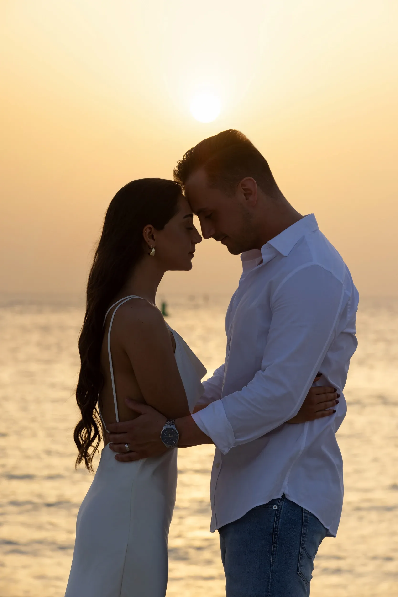 A couple touching foreheads against a golden sea at sunset.