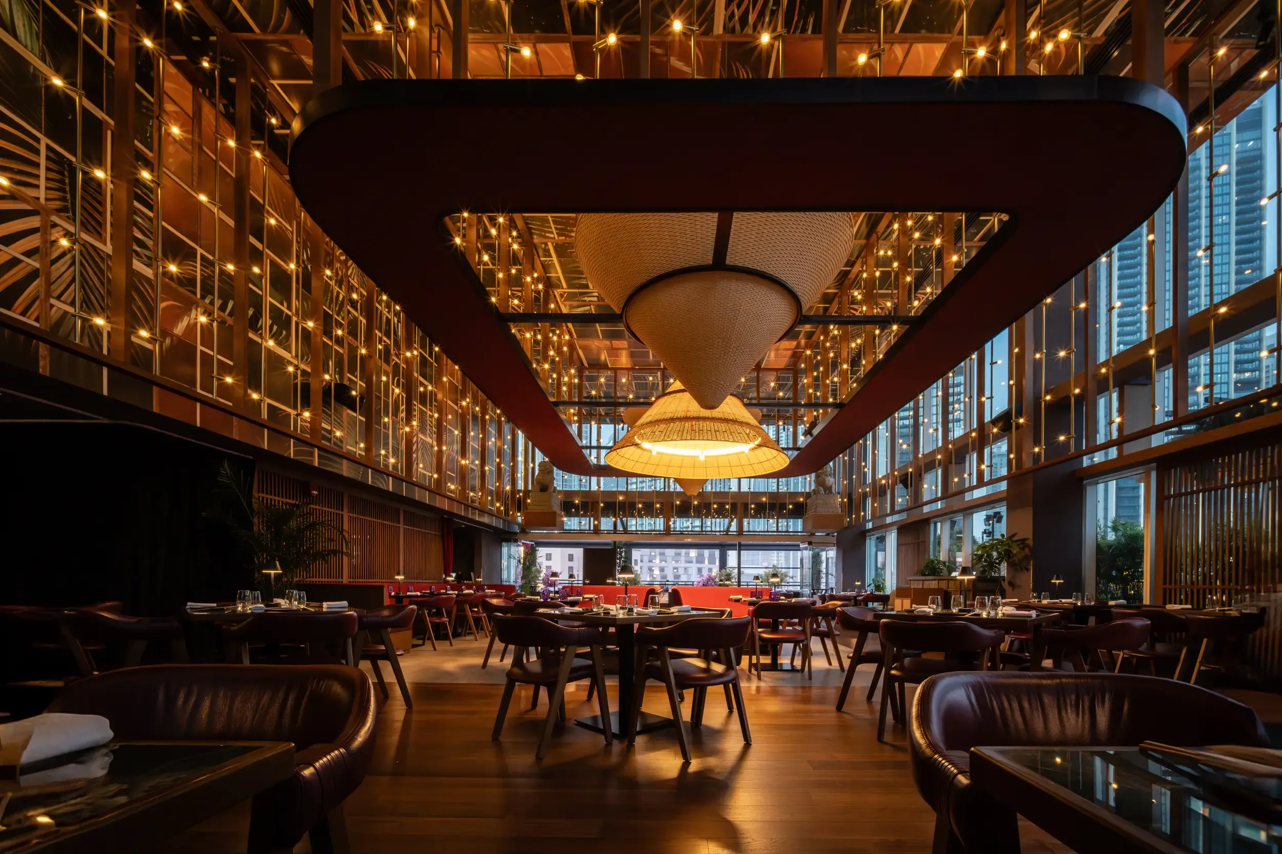 A symmetrical restaurant interior with warm illuminated shelving and a large central ceiling feature.