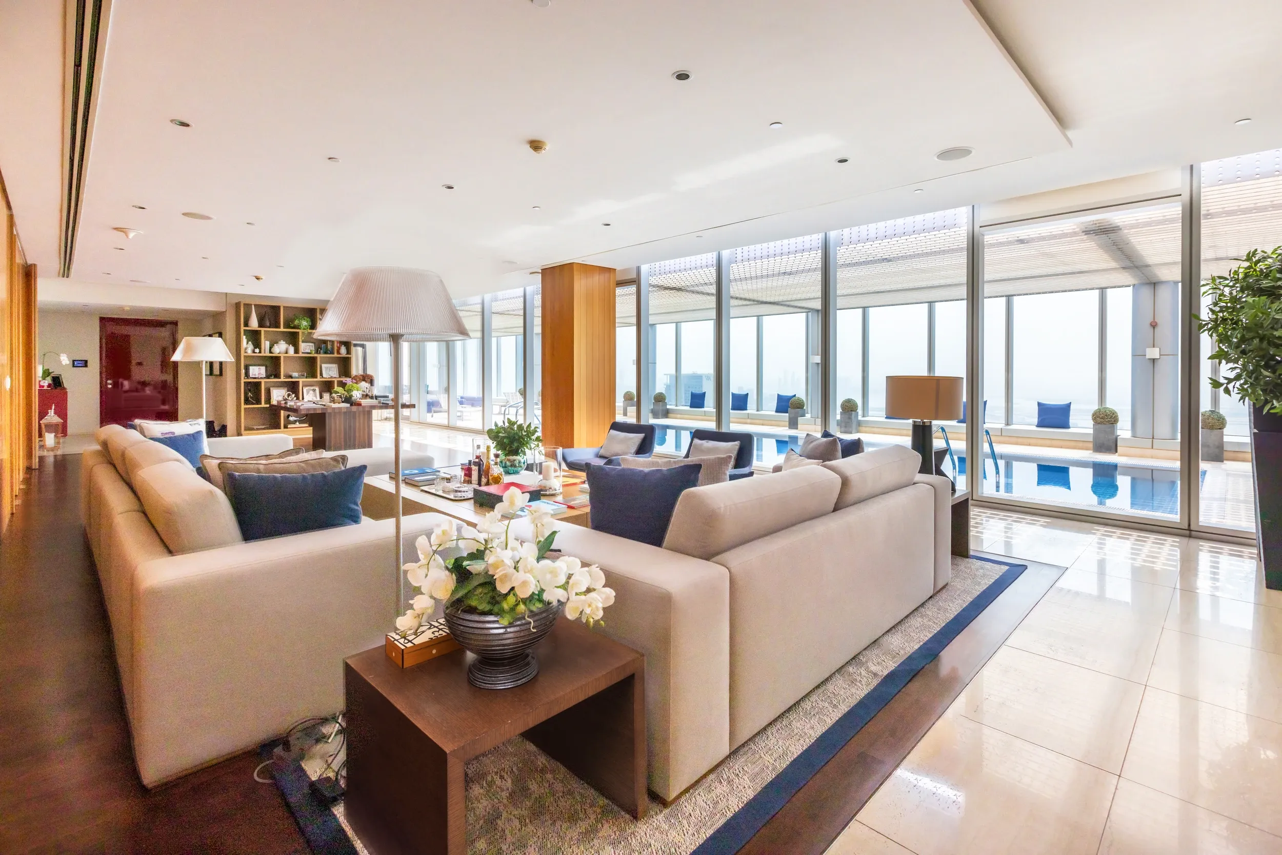 A bright lounge with pale sofas opening visually onto an indoor swimming pool.