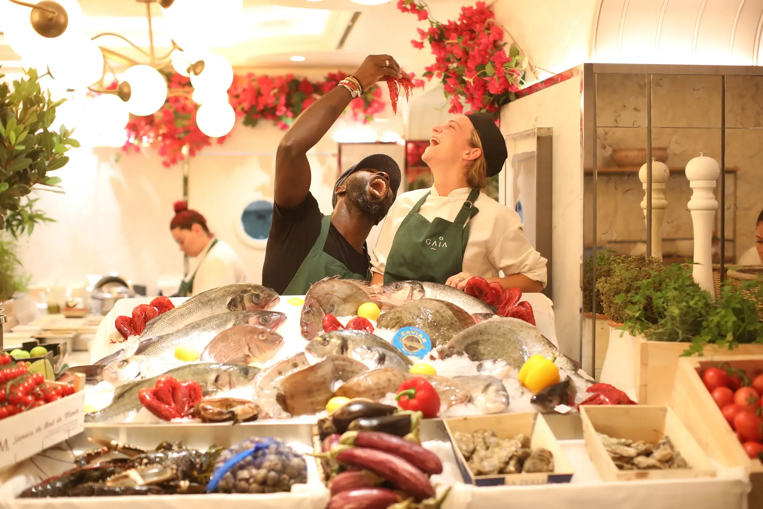 GAIA kitchen staff laughing behind a tiered ice seafood display with caviar label, oysters and pink bougainvillea