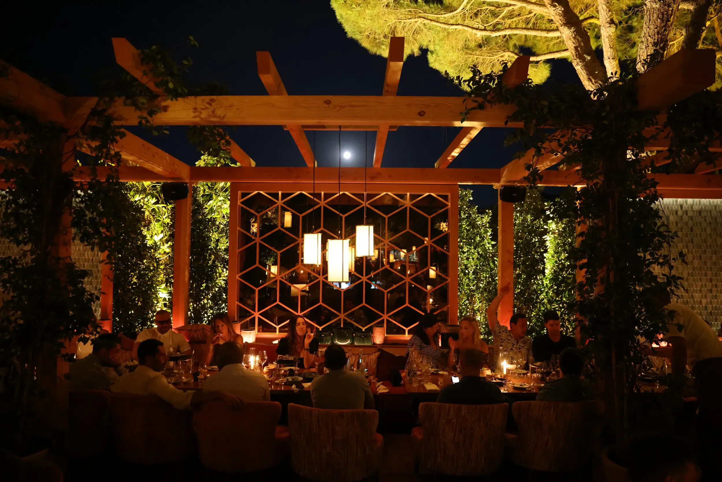 Long outdoor dinner under a vine-wrapped Kinugawa pergola with hanging lanterns and a full moon between beams