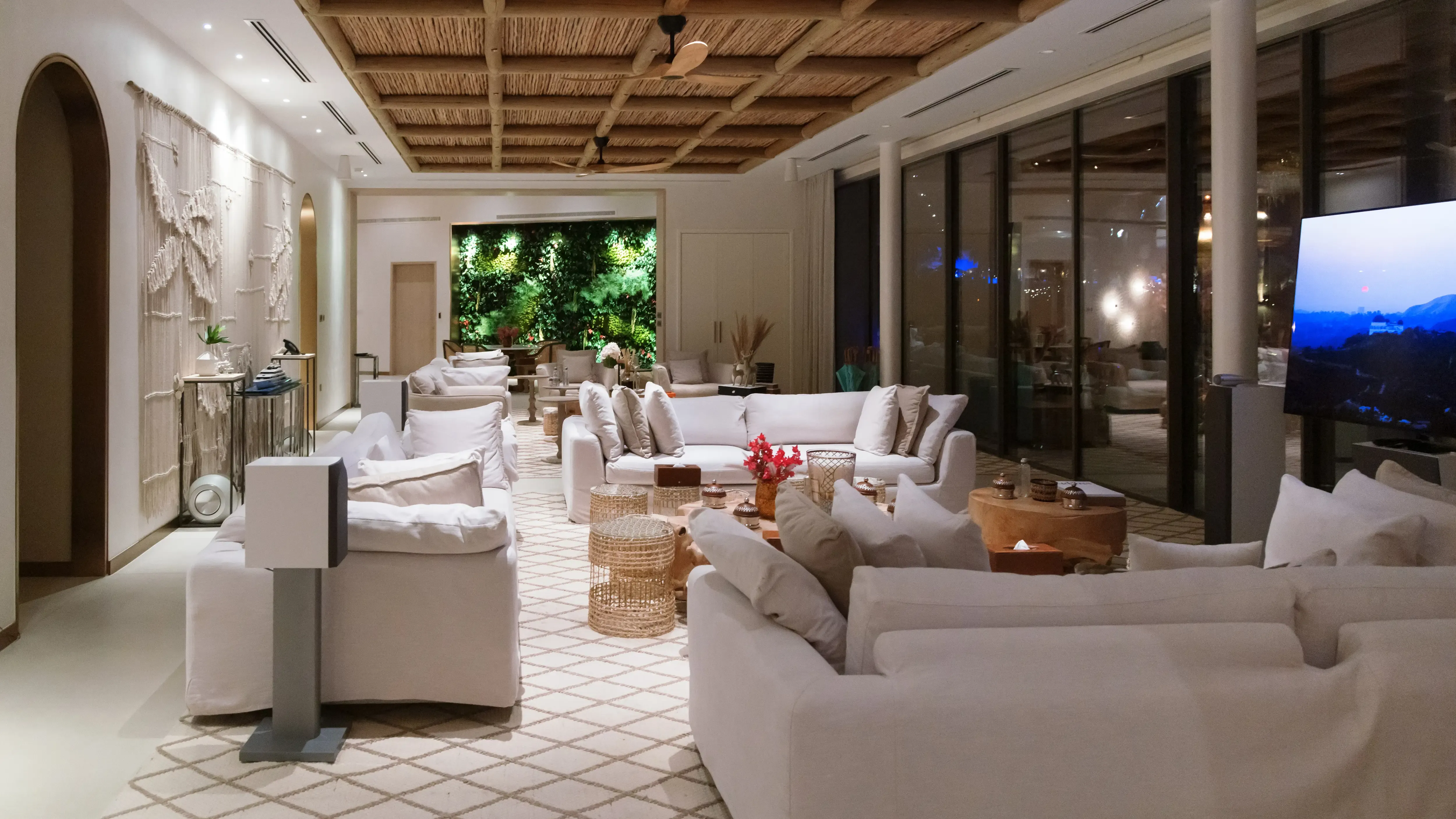 Night interior of a luxury villa lounge with white sofas, wooden grid ceiling and living green wall