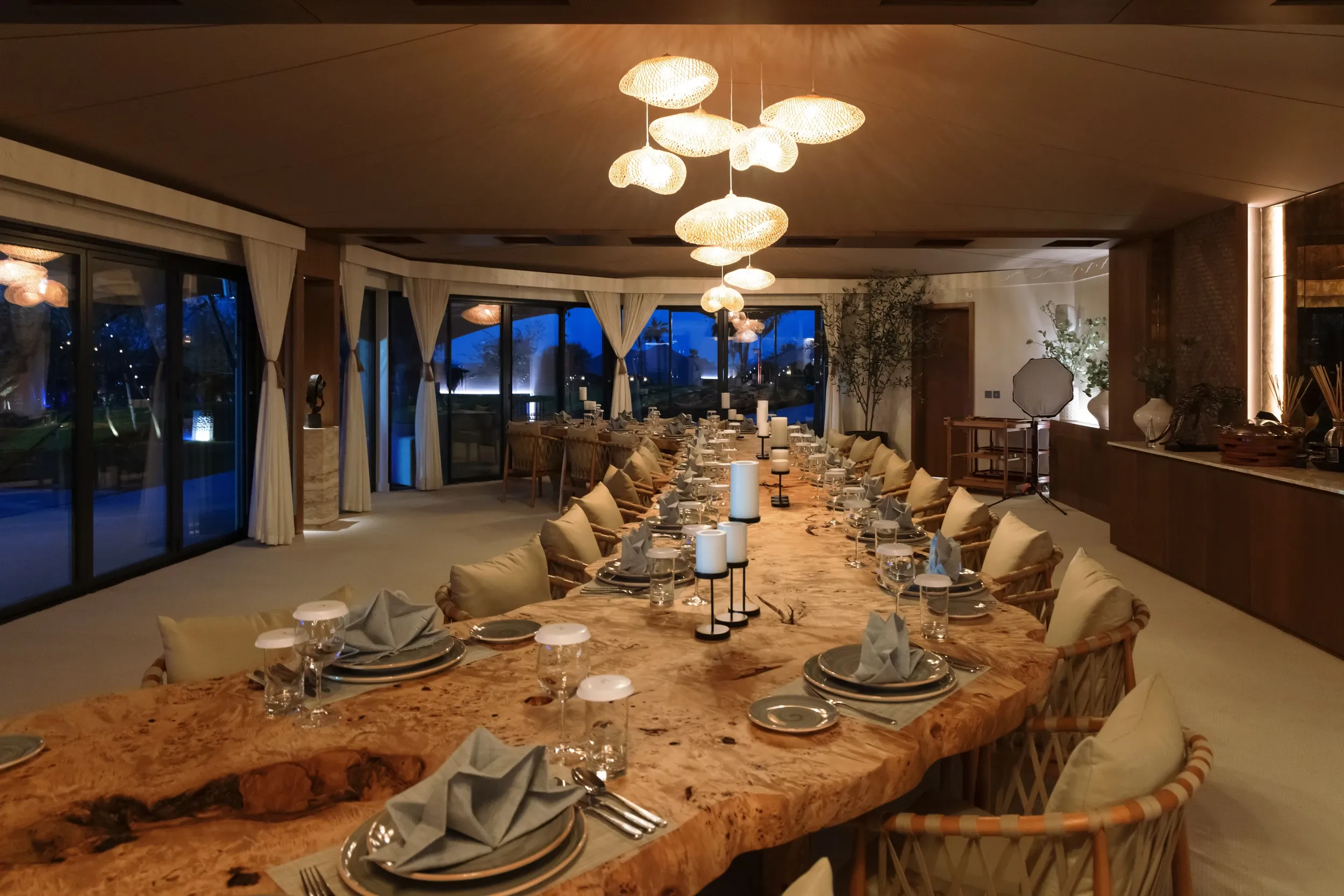 A long natural-edge dining table set for an evening gathering beneath warm pendant lights.