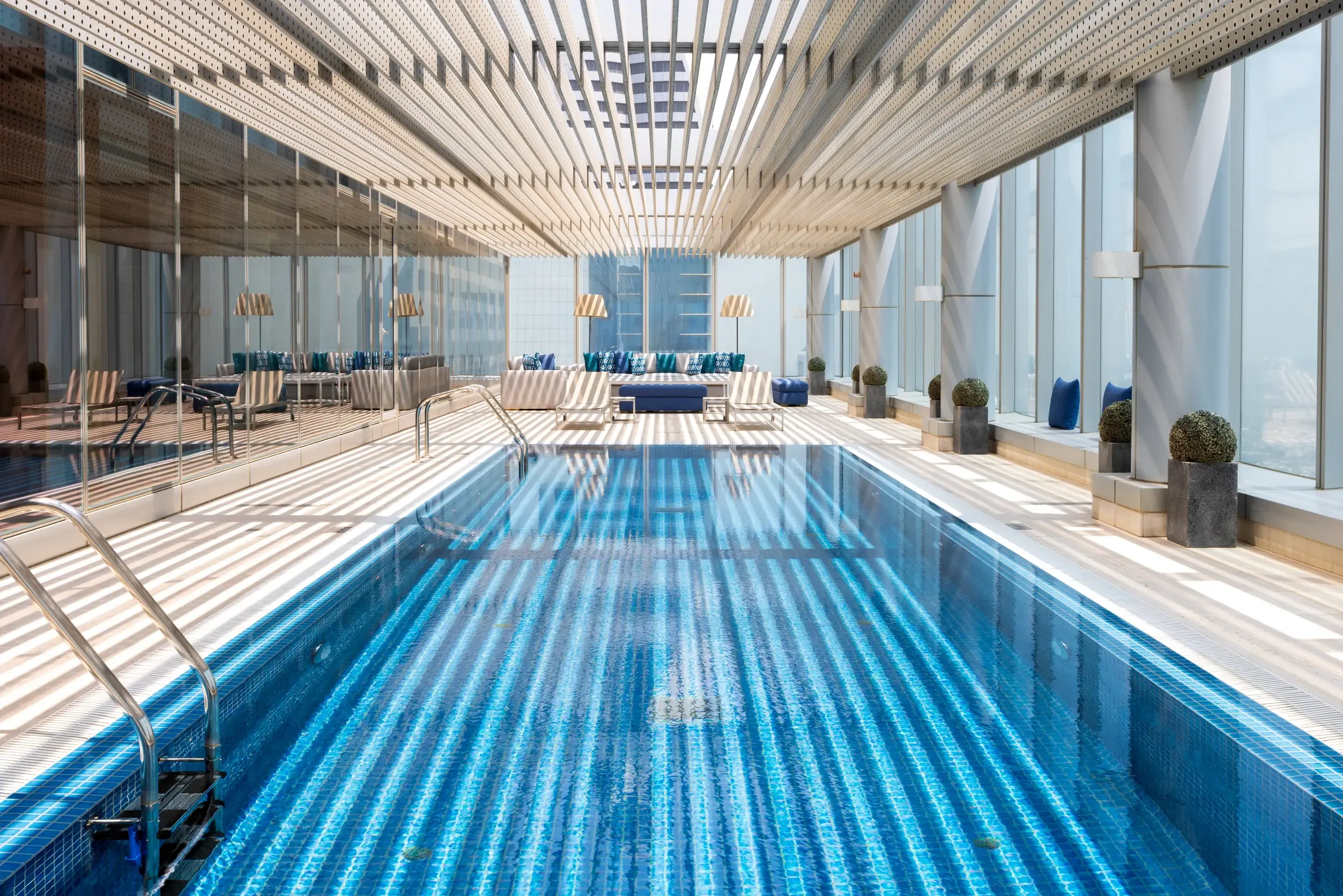 Rolex Tower indoor lap pool with slatted ceiling light stripes, blue mosaic and Dubai skyline beyond