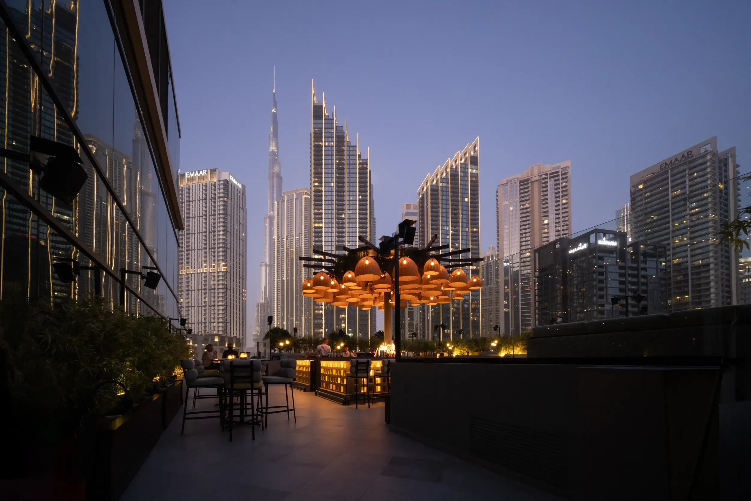Blue-hour rooftop lounge with rattan pendant canopy and Burj Khalifa / Emaar skyline