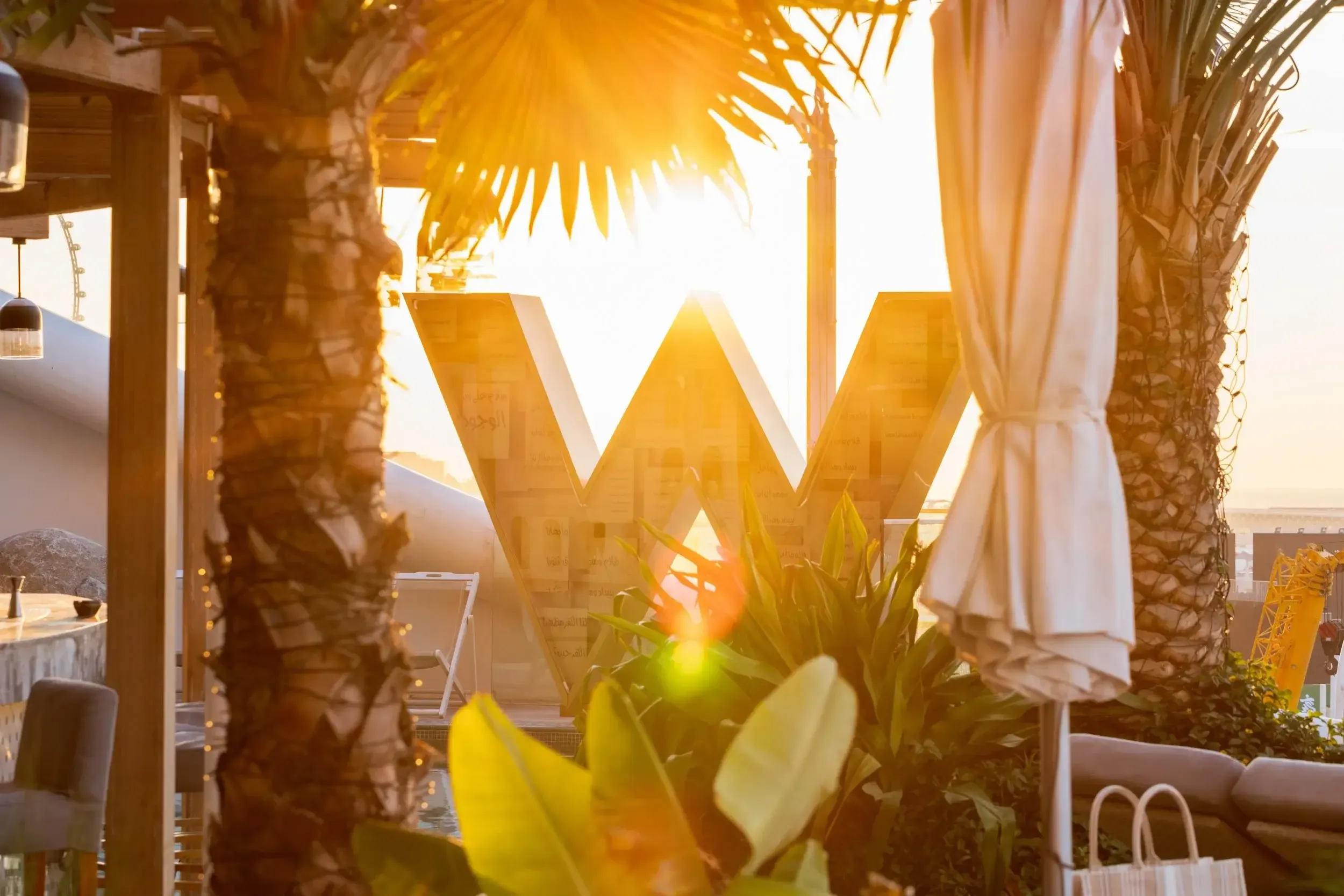Golden-hour backlight through the W Hotels logo sculpture at W Dubai The Palm with Palm Jumeirah skyline
