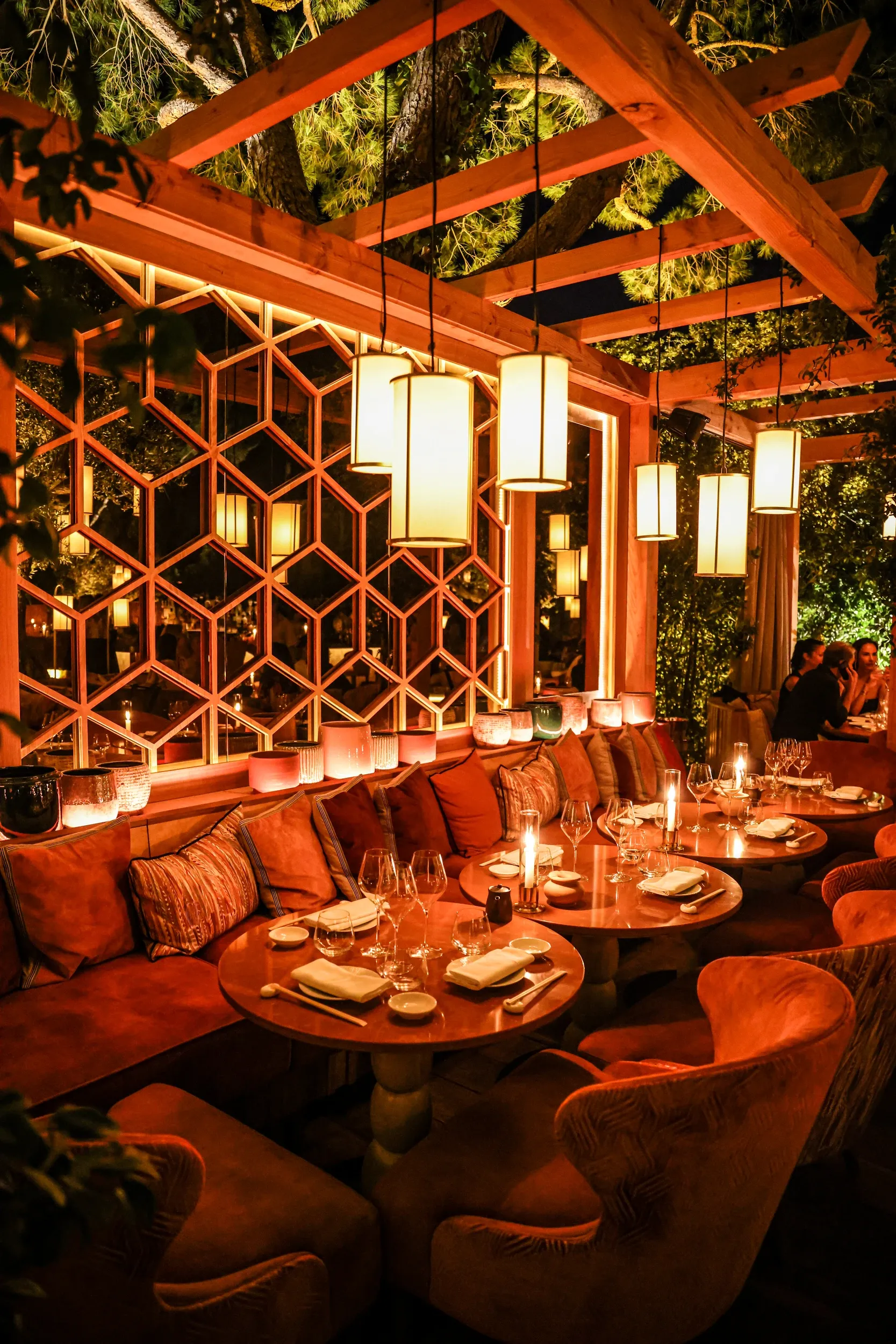 An intimate restaurant seating area beneath a timber pergola and hanging lanterns.