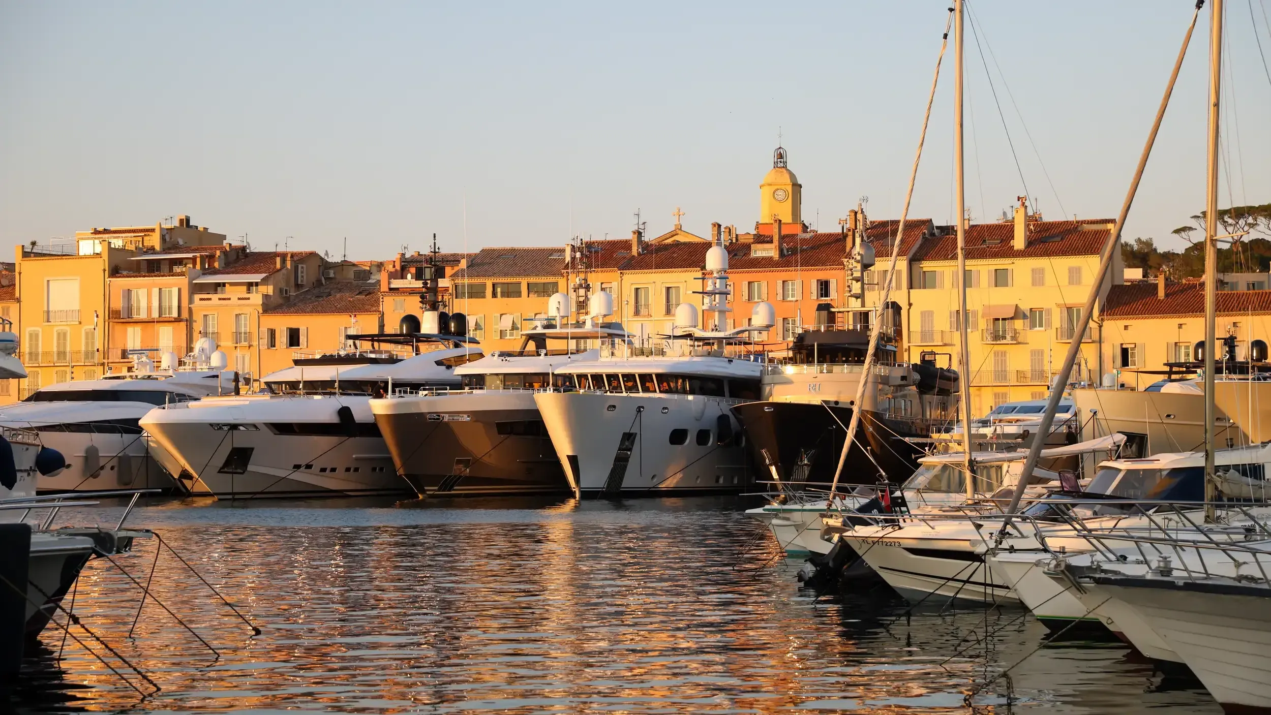 Saint-Tropez harbour at golden hour with superyachts and the clock tower