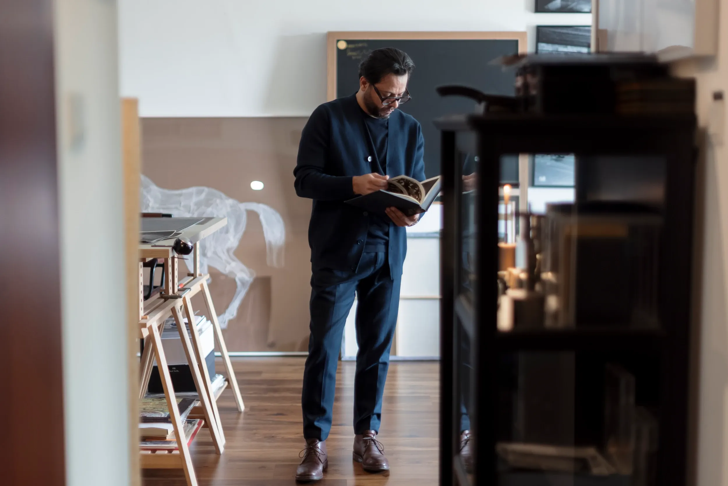 A man reading a book in a studio, framed by furnishings in the foreground.