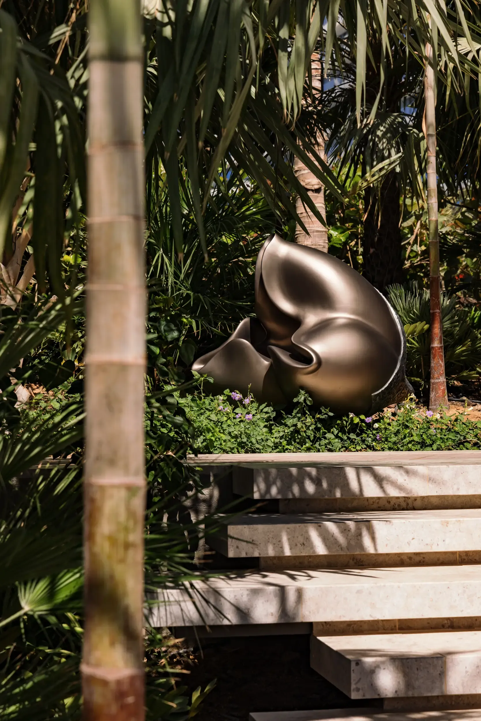 Abstract bronze organic sculpture among tropical foliage beside stone garden steps