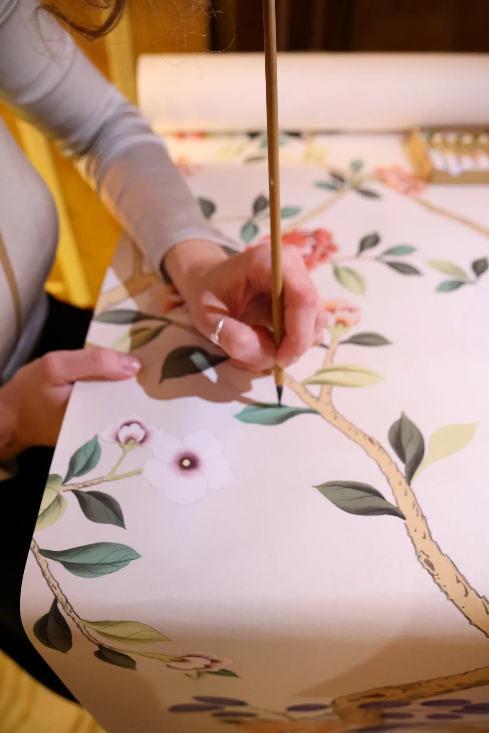 Hands painting floral details onto a pale pink surface.