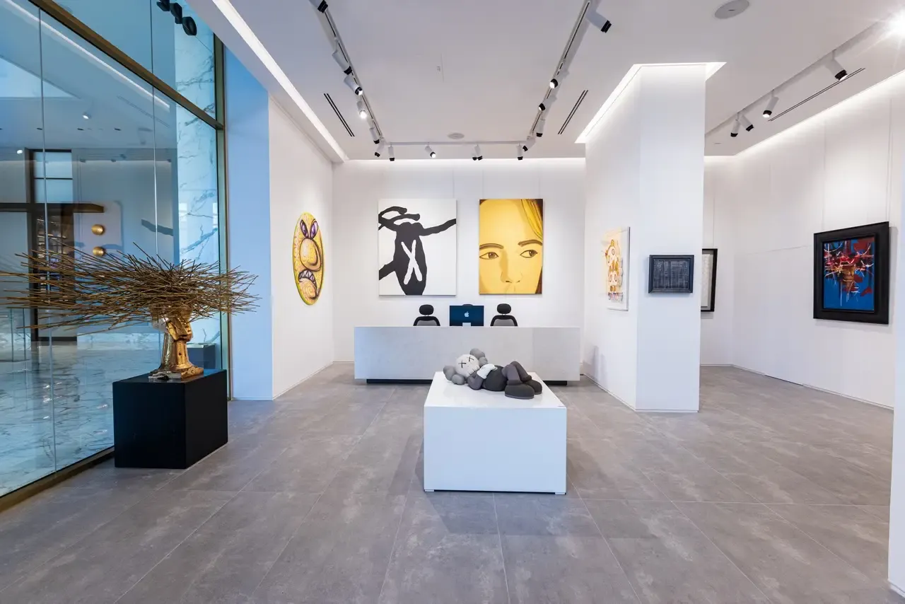 Bright contemporary gallery lobby with KAWS-style sculpture, gold bust, and large canvases at a reception desk