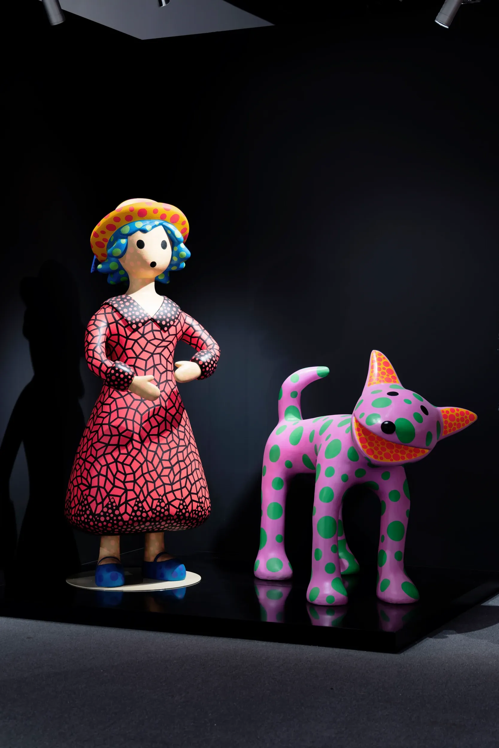 Colourful sculptures of a woman and a spotted animal displayed against a dark wall.